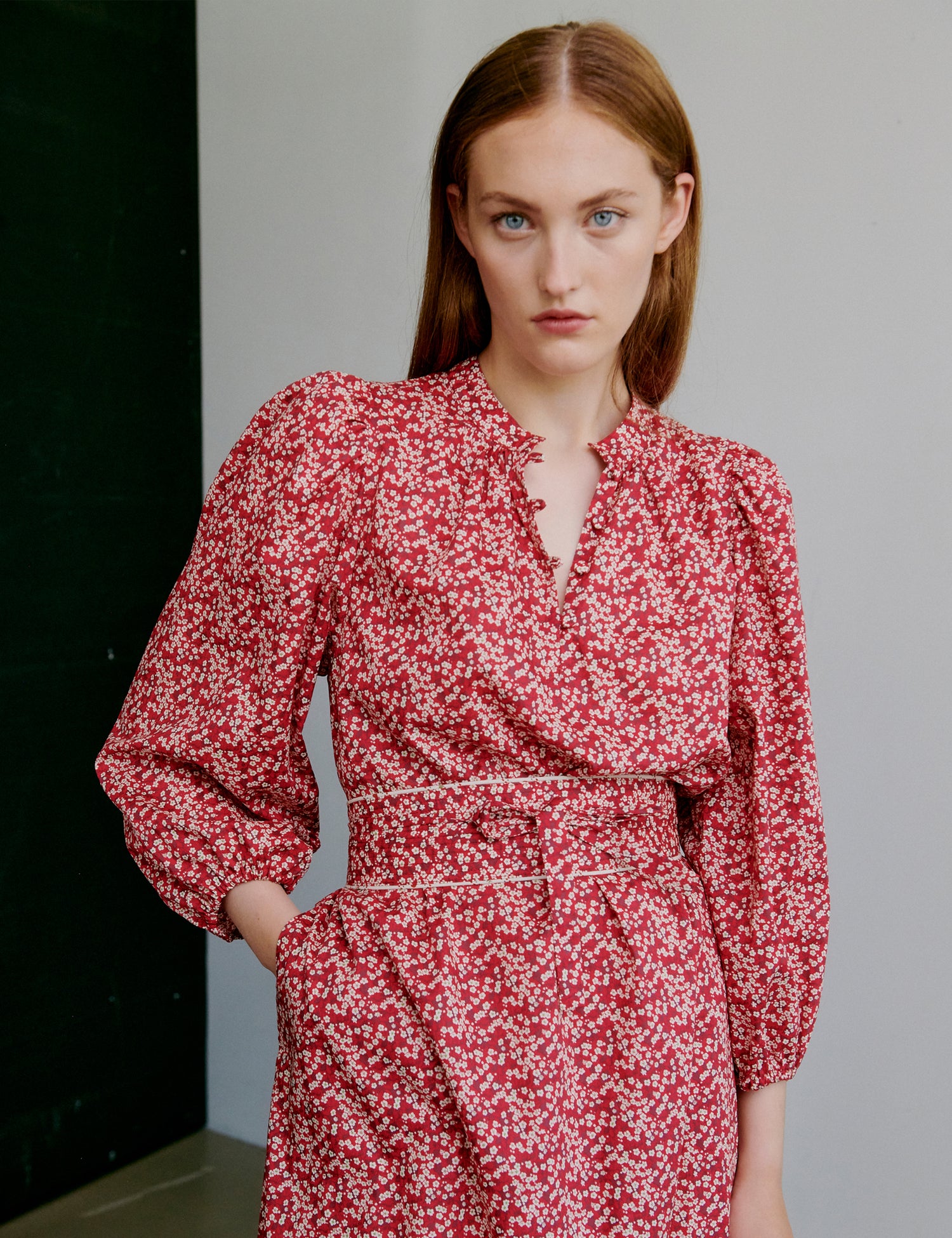 Woman wearing a red floral dress with long puff sleeves, round collar with covered buttons and matching fabric belt