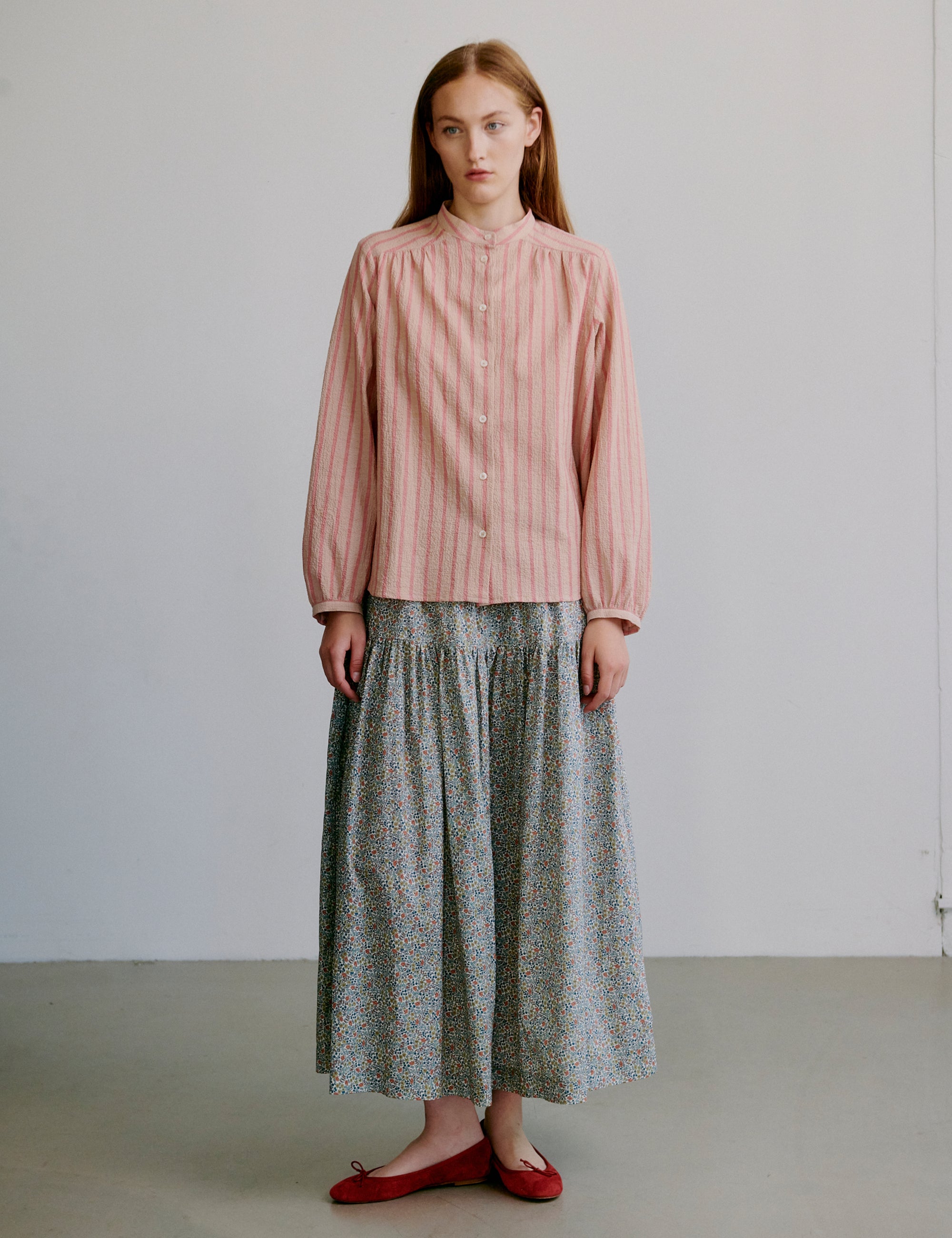 Woman wearing a pink striped long sleeve shirt and flower patterned skirt against a plain background
