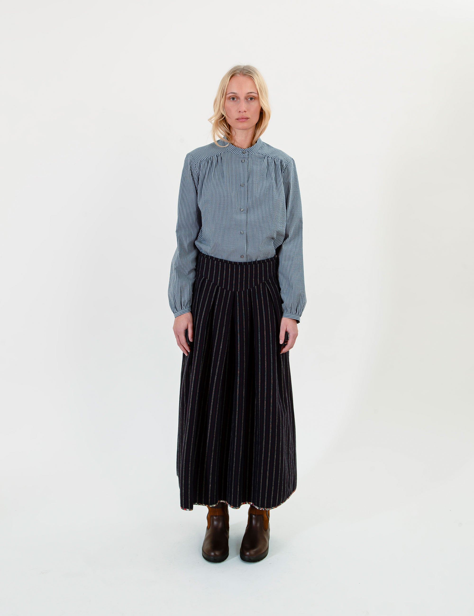 Woman wearing a blue shirt and black pleated and striped skirt on a white background