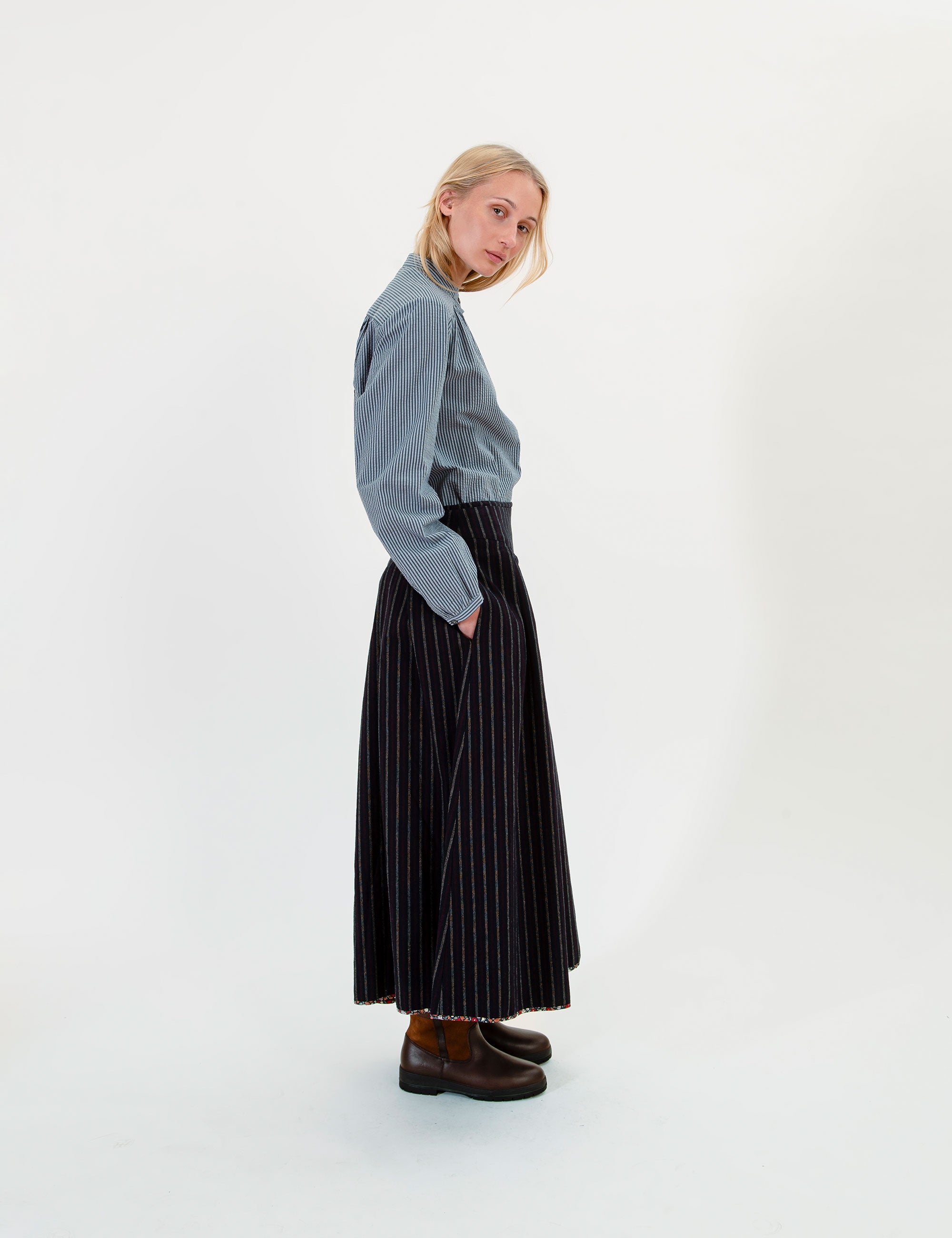 Woman wearing a blue shirt and black pleated and striped skirt on a white background