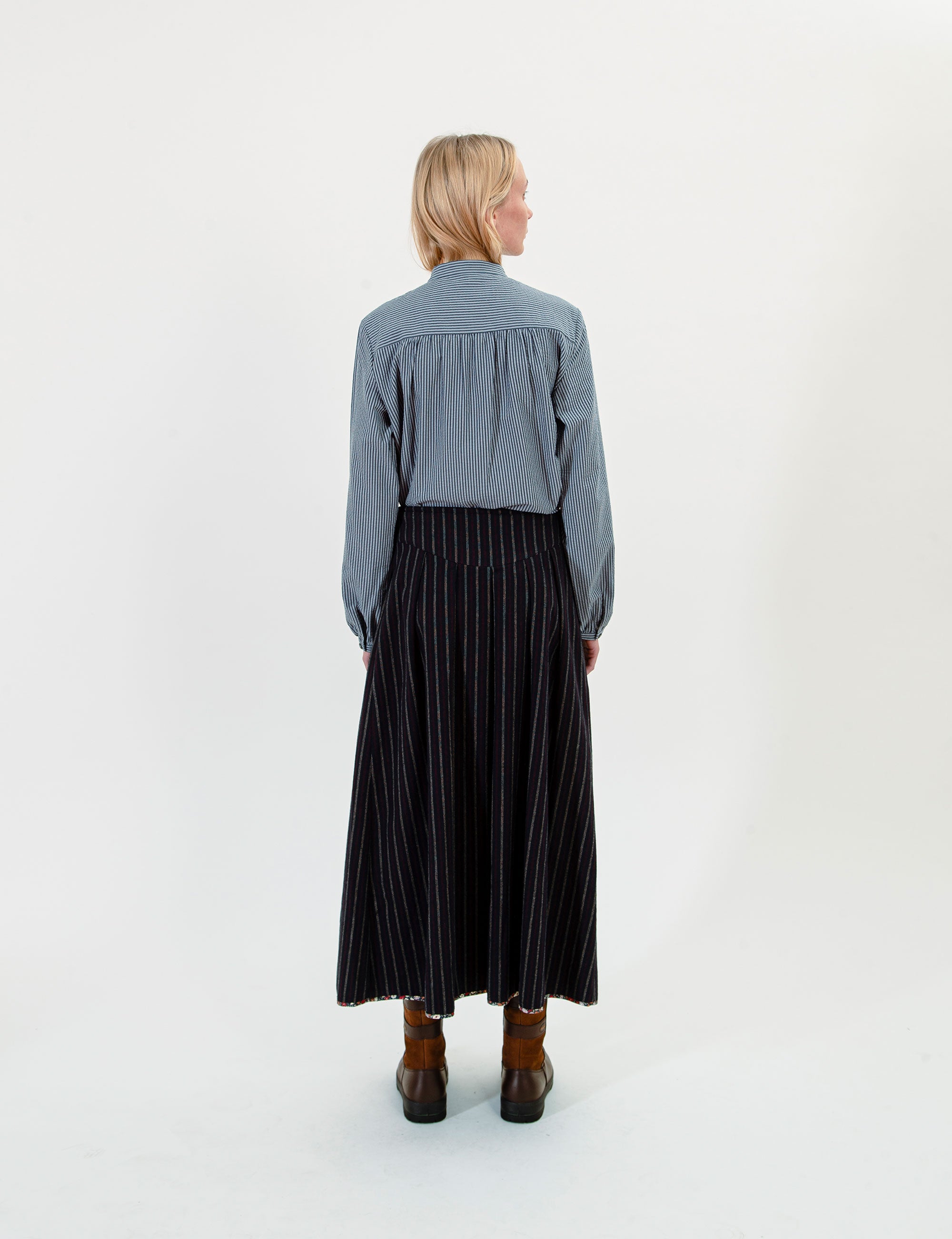 Woman wearing a blue shirt and black pleated and striped skirt on a white background