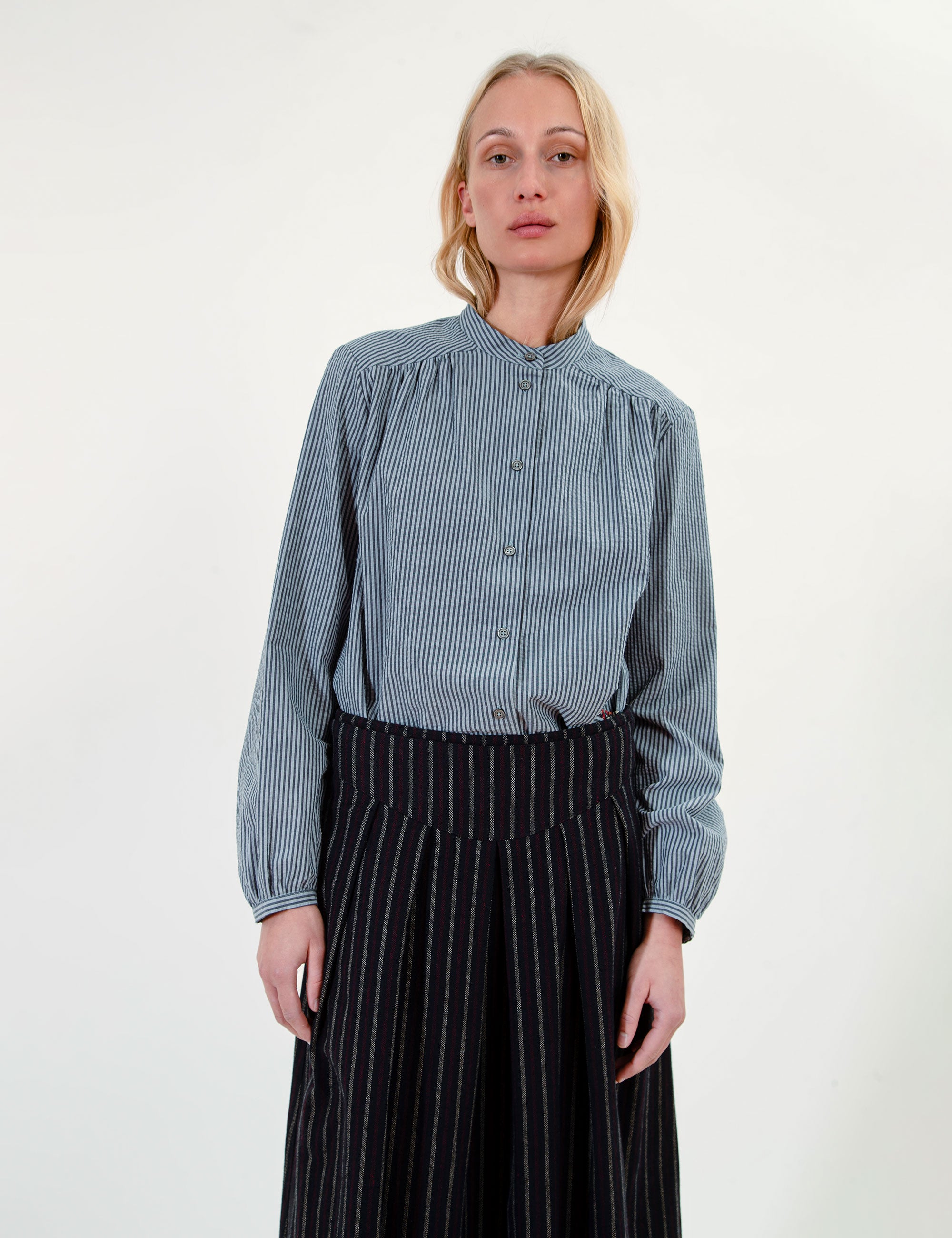 Woman wearing a blue shirt and black pleated striped skirt on a white background