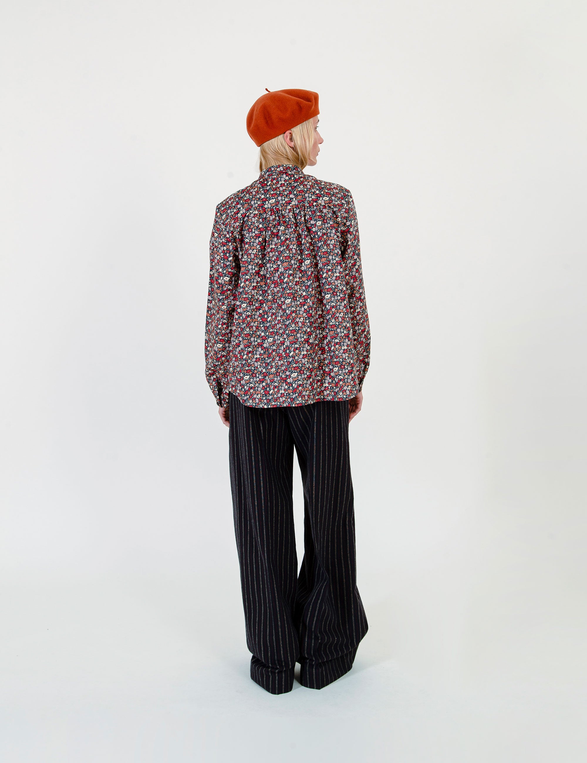 Woman wearing a flower patterned blouse and black striped pants with a orange beret