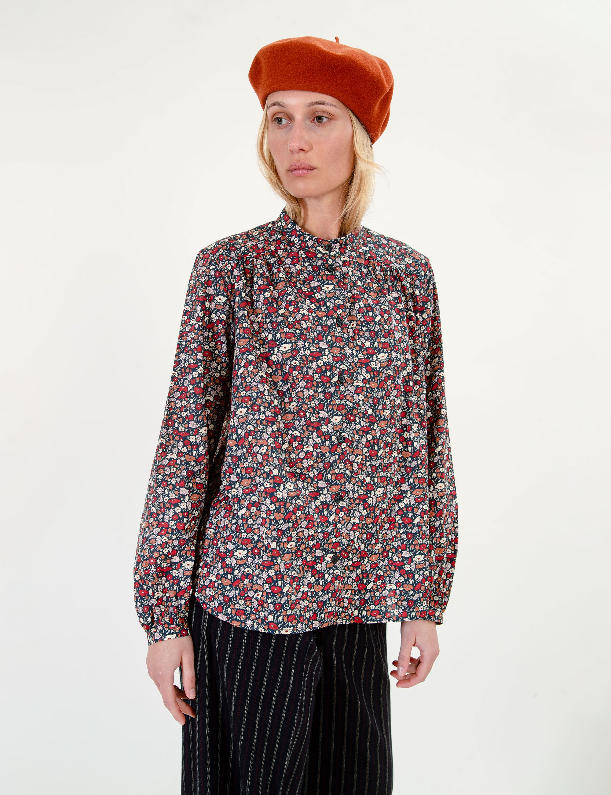 Woman wearing a flower patterned blouse and black striped pants with a orange beret