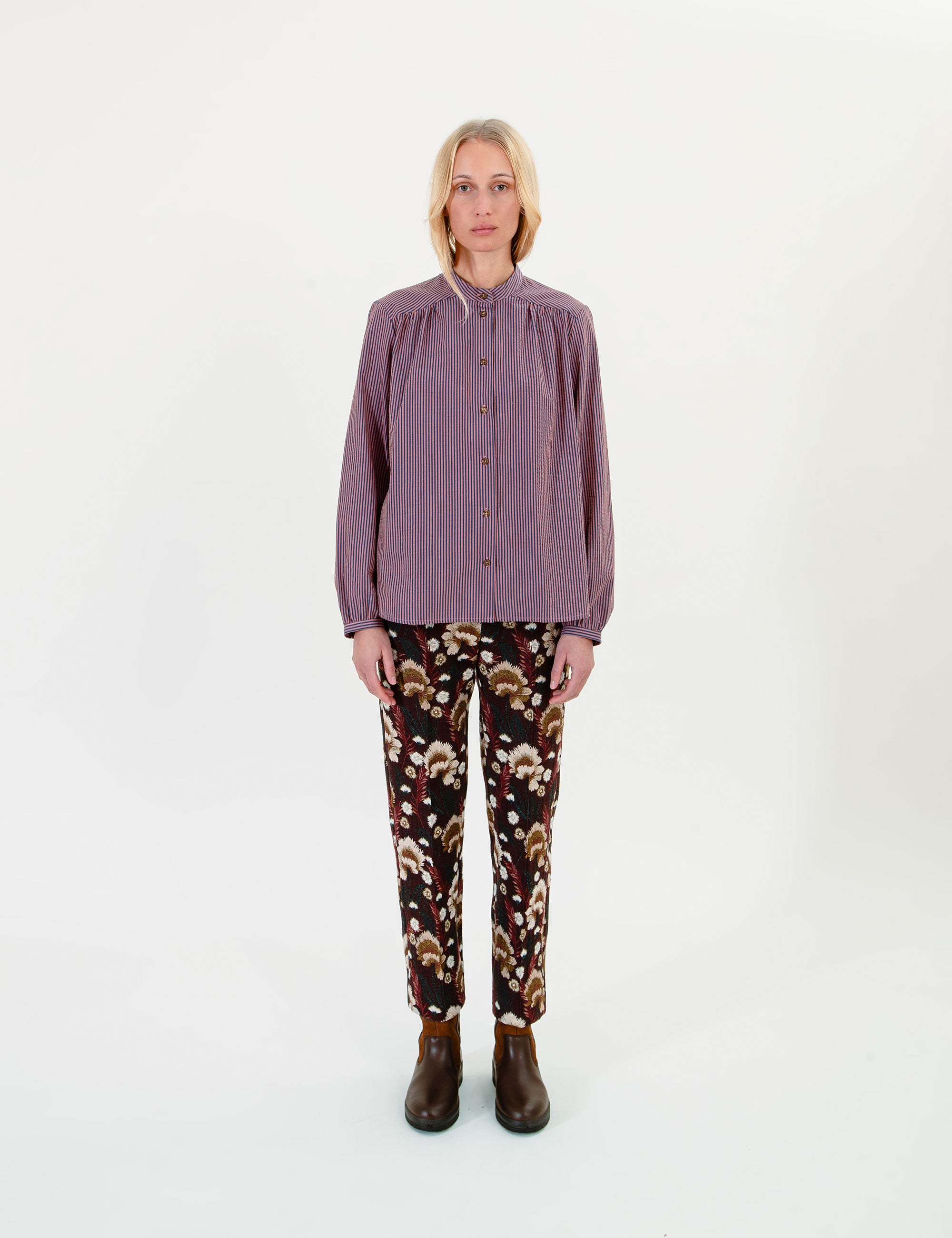 Woman wearing a long-sleeve striped purple shirt and brown patterned pants on a white background
