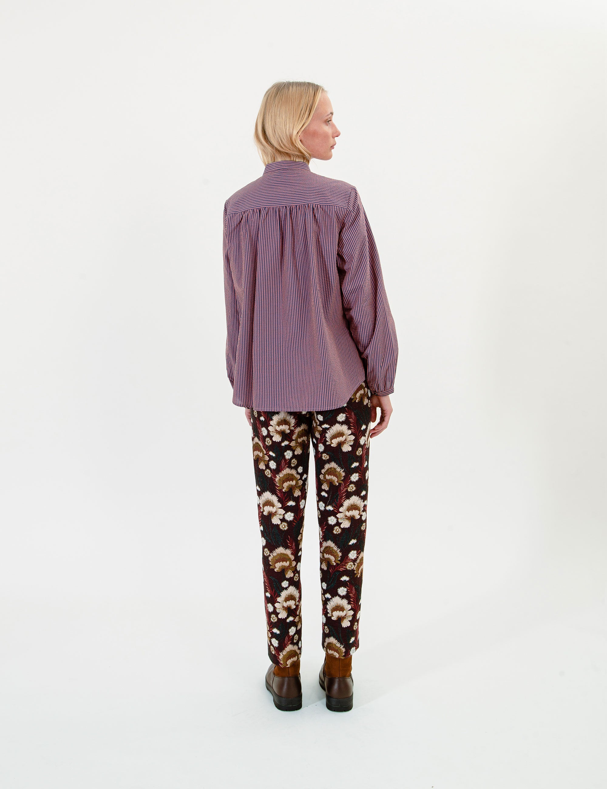 Woman wearing a long-sleeve striped purple shirt and brown patterned pants on a white background