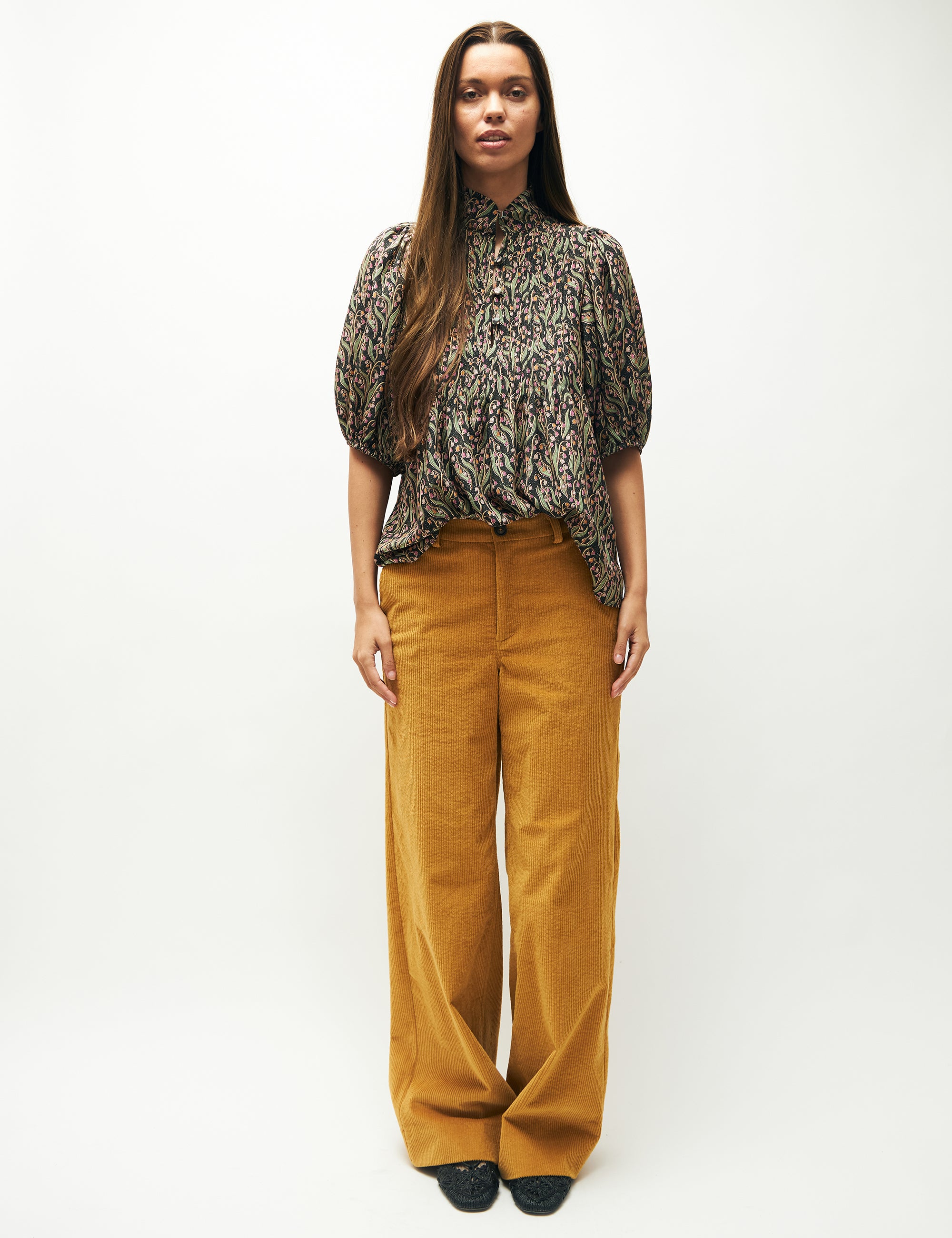 Woman in wide yellow corduroy pants and pink and green flower patterned blouse with short sleeves