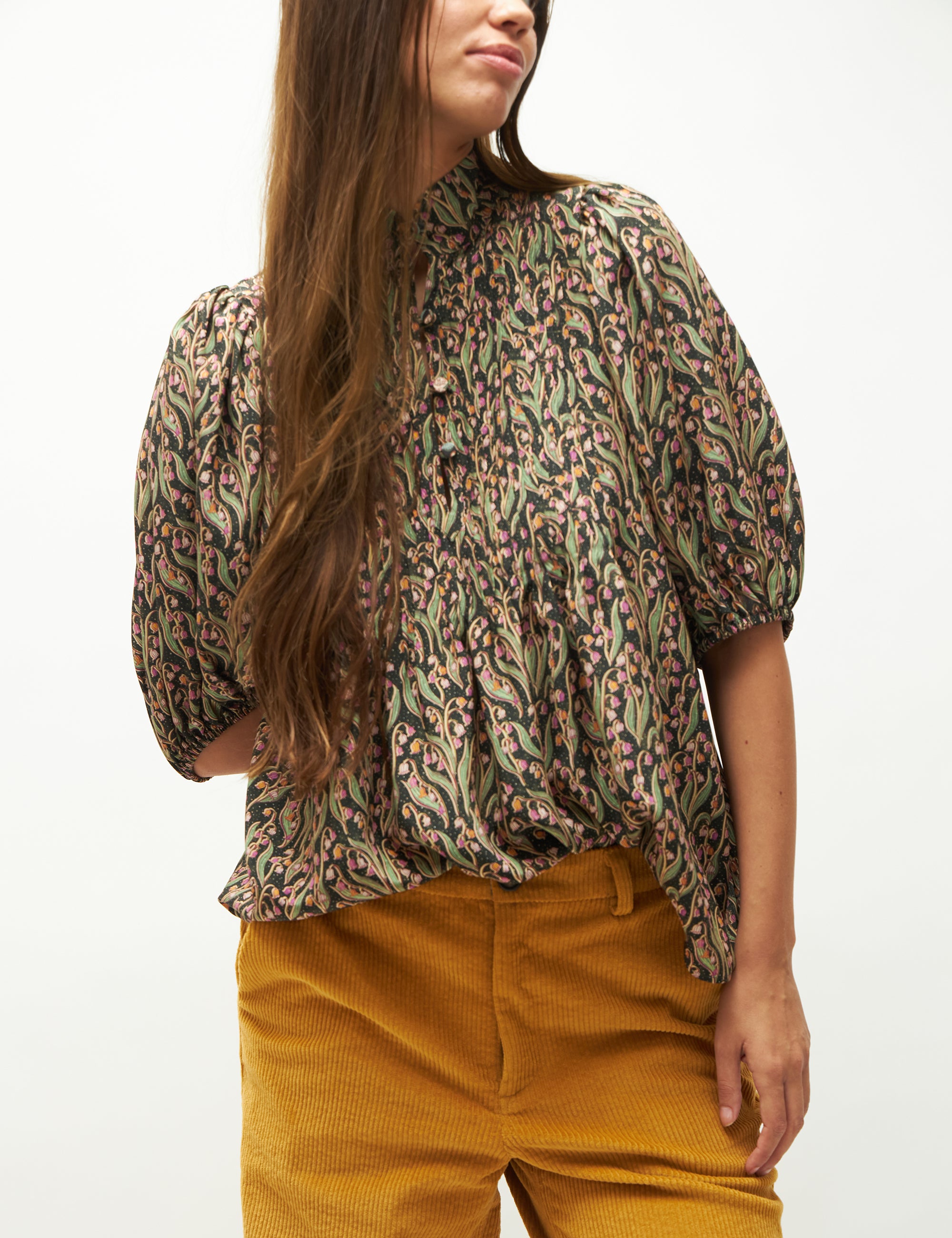 Woman wearing a patterned blouse and mustard pants on a white background