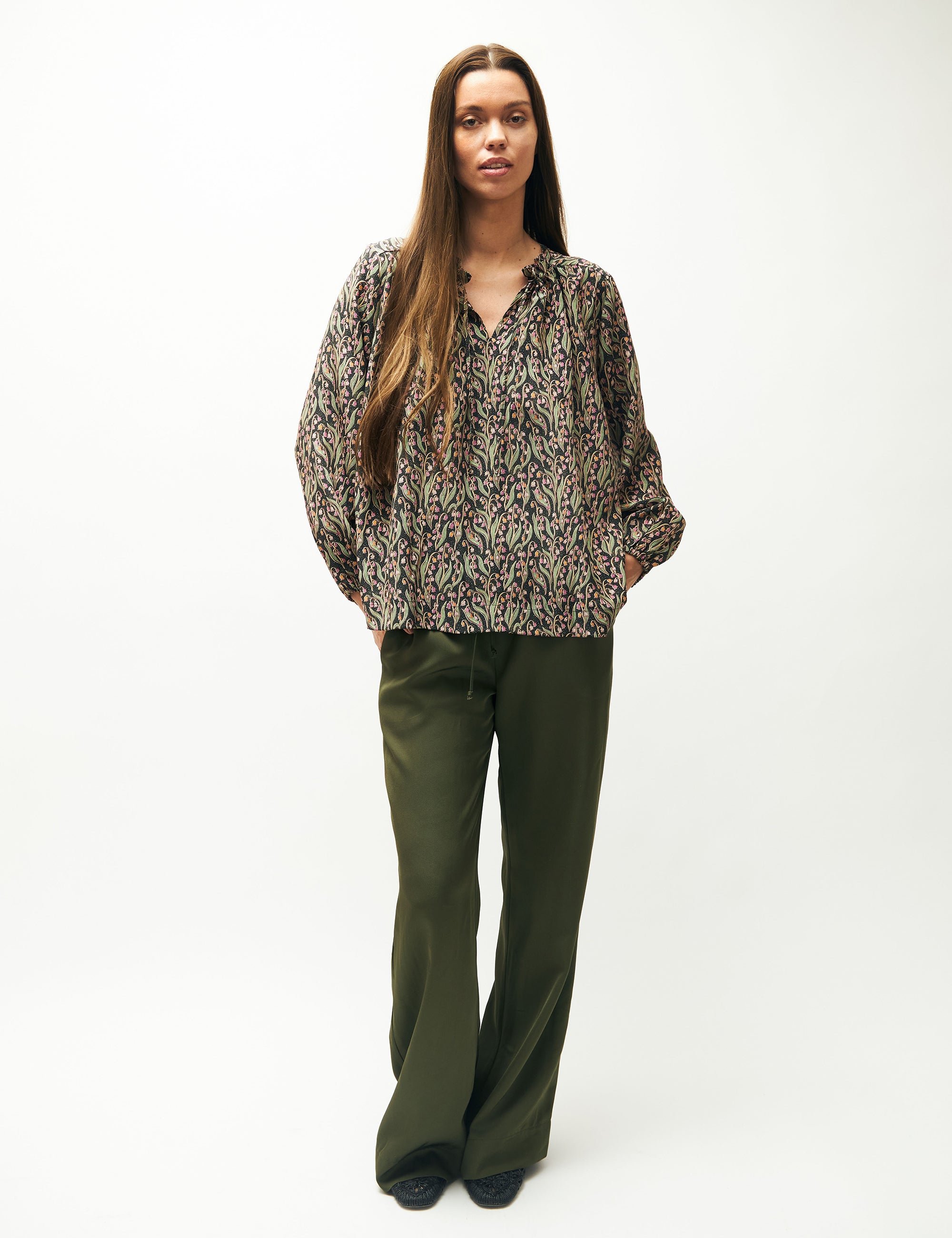 Woman in green pants and green and pink flower patterned shirt with long sleeves