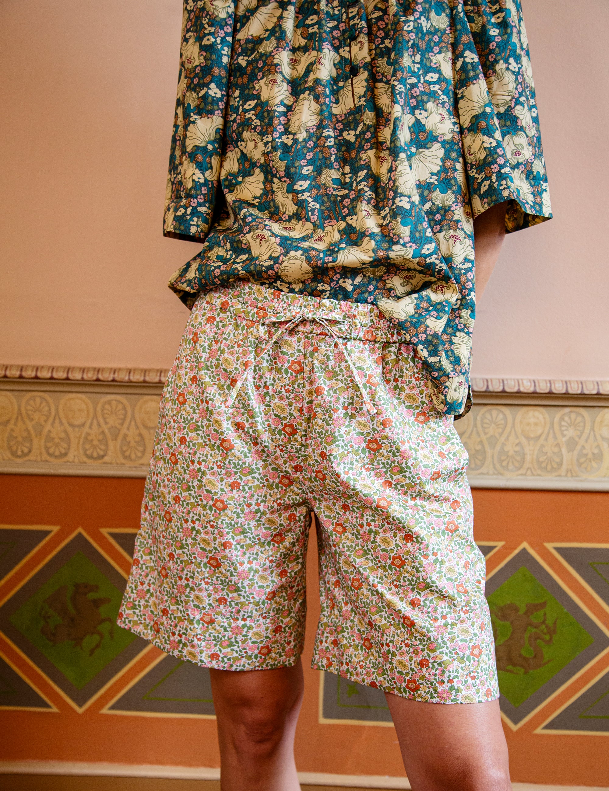 Floral patterned shirt and shorts on a person against a decorative wall.