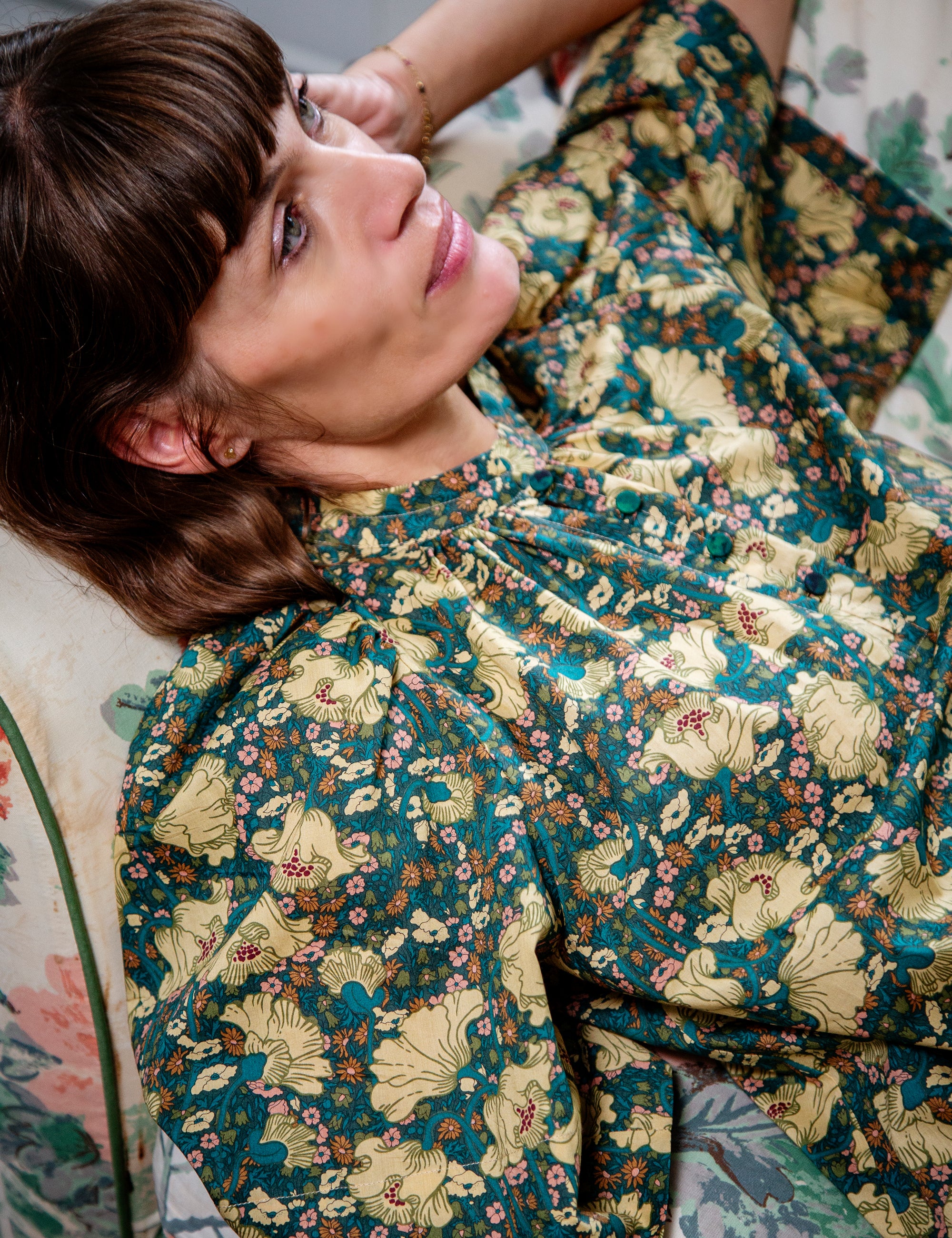 Woman wearing a floral patterned shirt sitting on a floral couch.