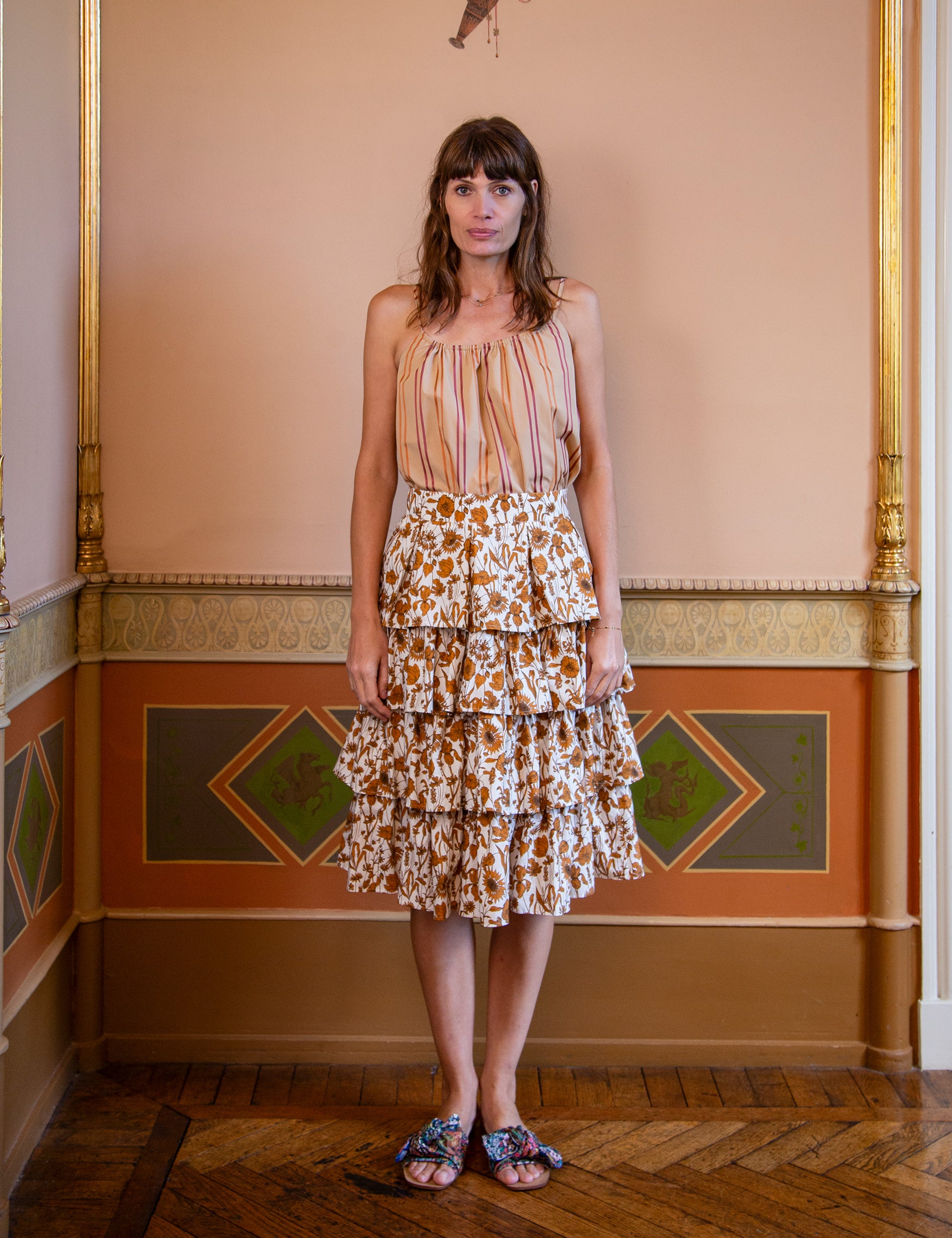 Woman wearing a striped strap top and a layered floral skirt in golden tones