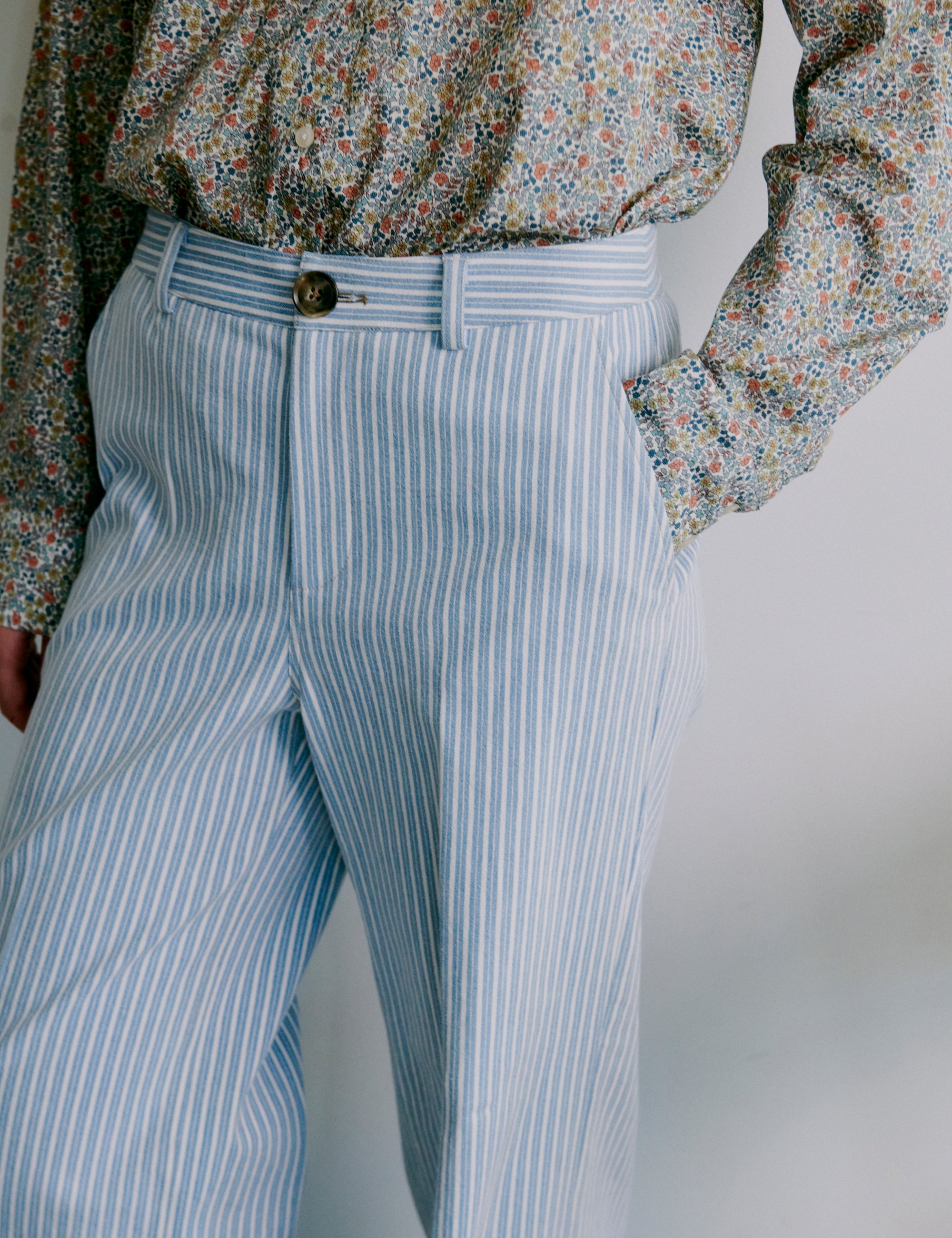 Woman wearing a floral patterned long sleeve shirt and light blue striped pants against a plain background