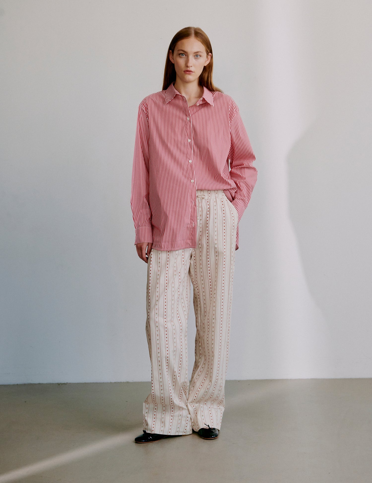Woman wearing a red striped long sleeve shirt and beige patterned pants against a plain background