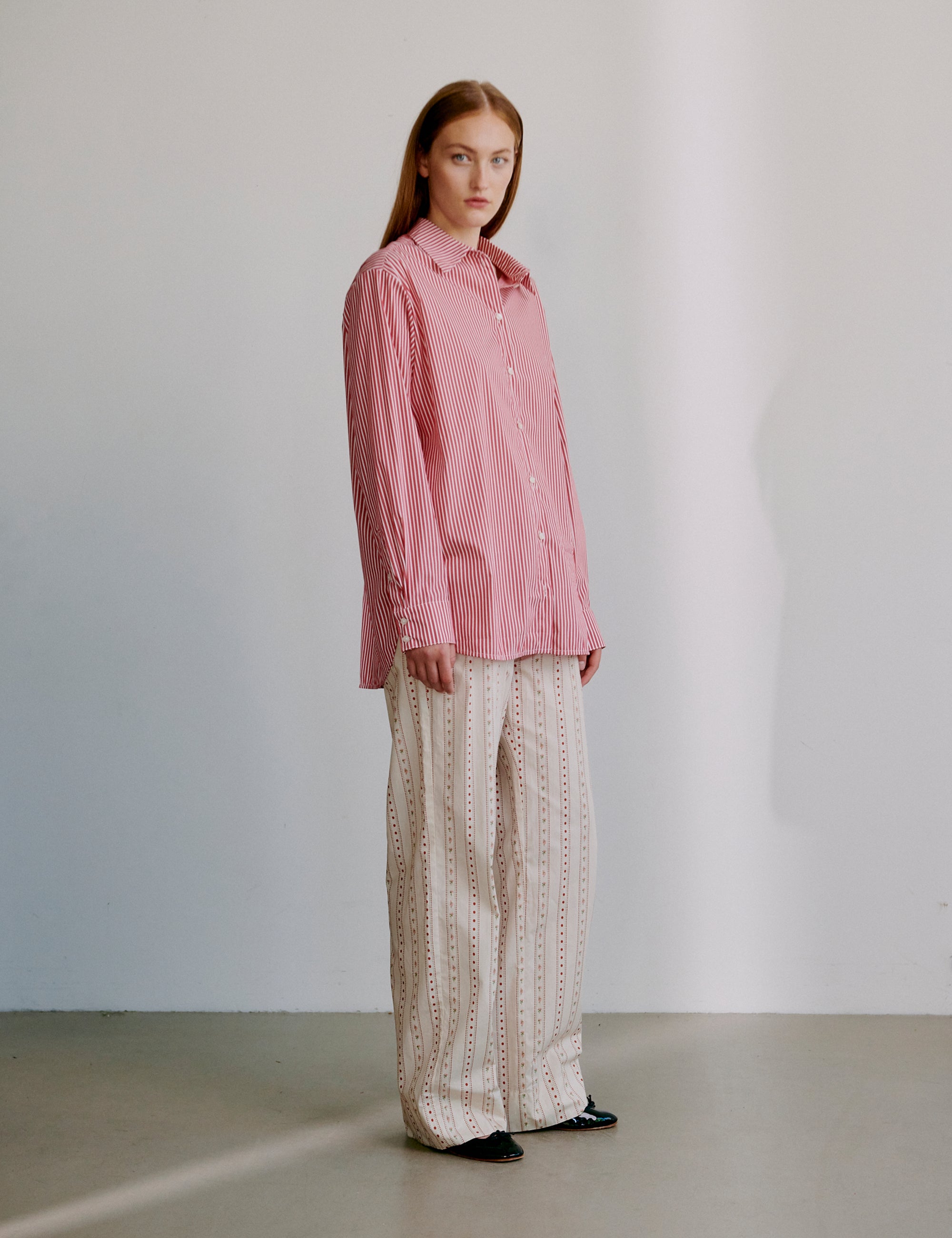 Woman wearing a red striped long sleeve shirt and beige patterned pants against a plain background
