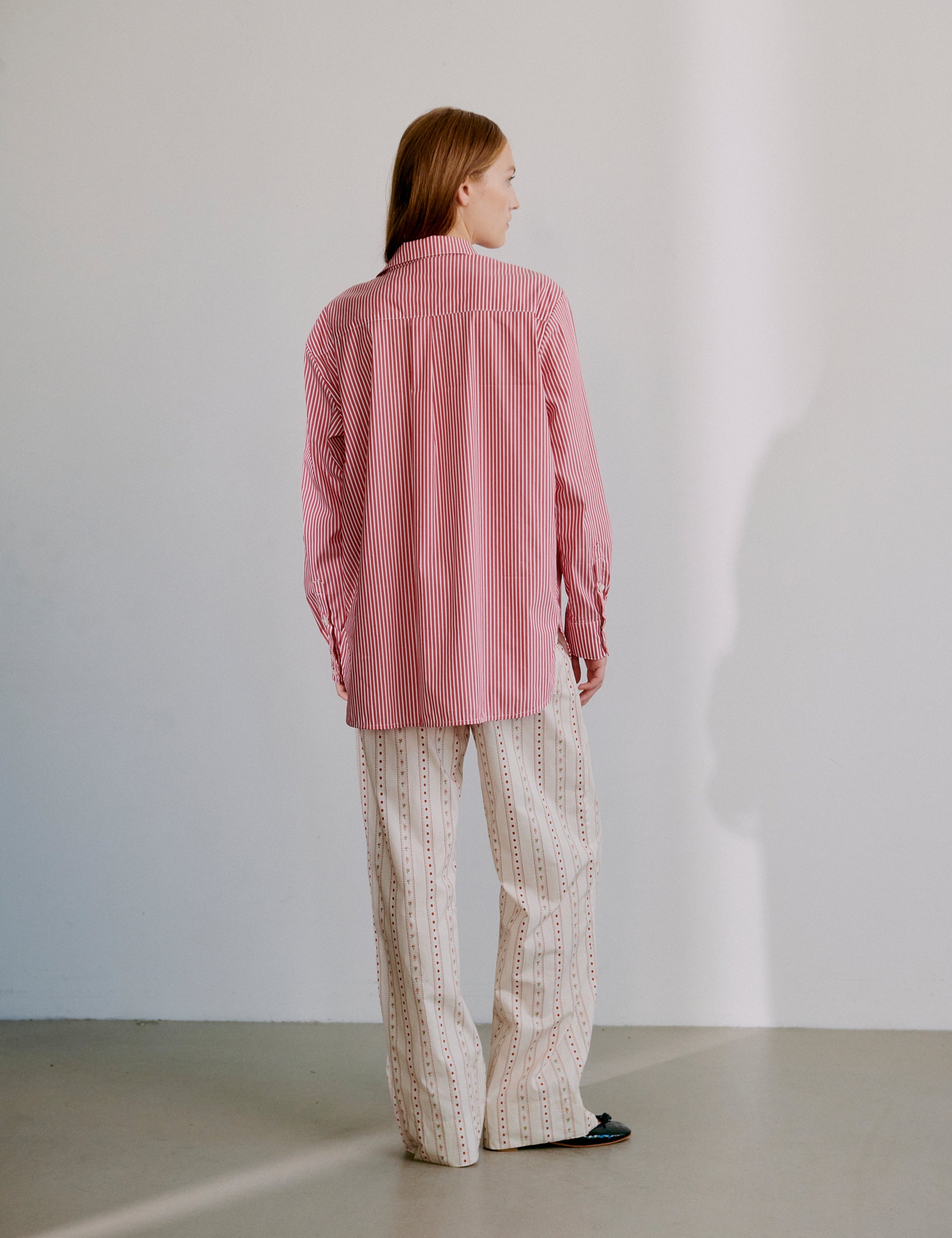 Woman wearing a red striped long sleeve shirt and beige patterned pants against a plain background