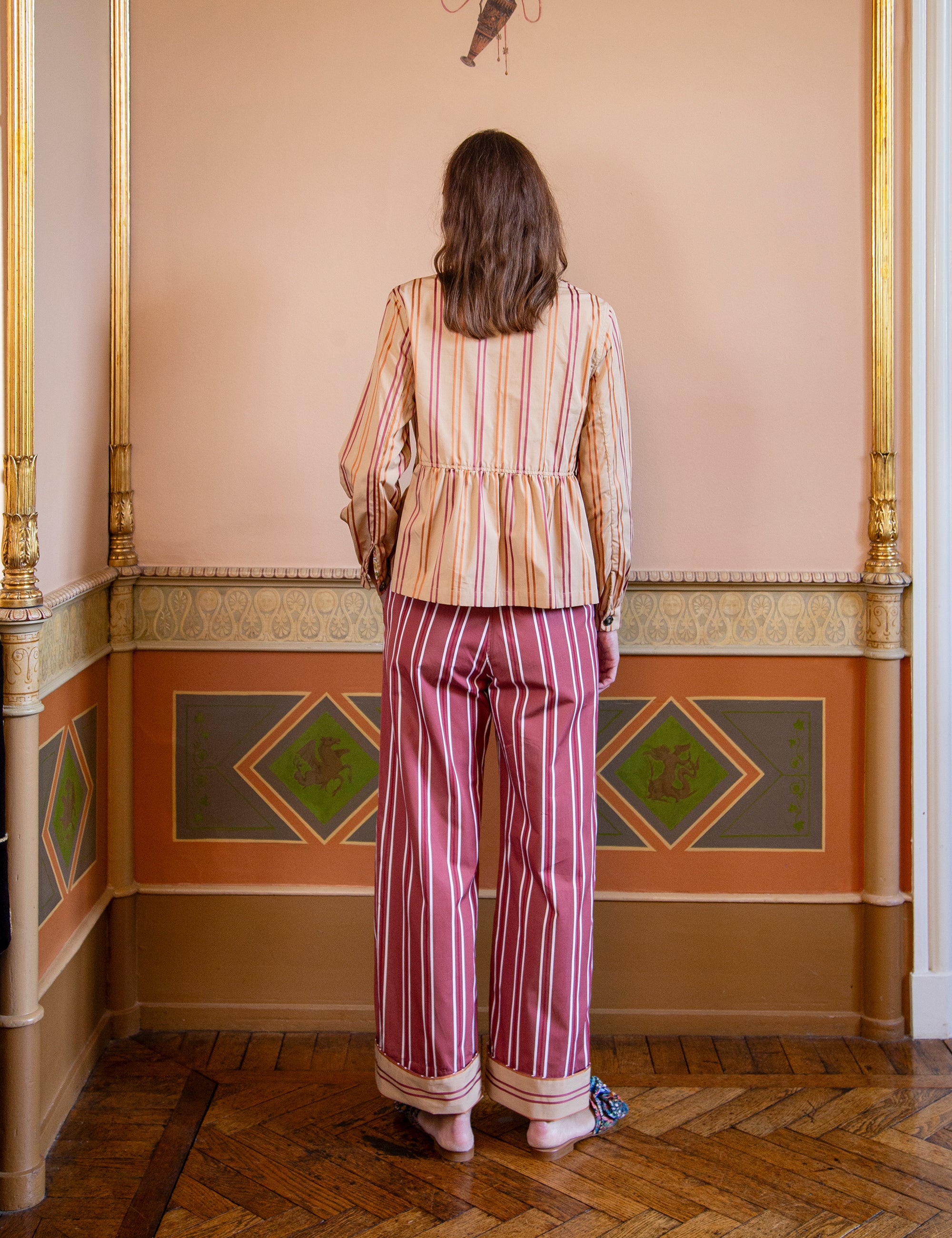 Woman in a striped outfit standing in a room with decorative walls and wooden floor.