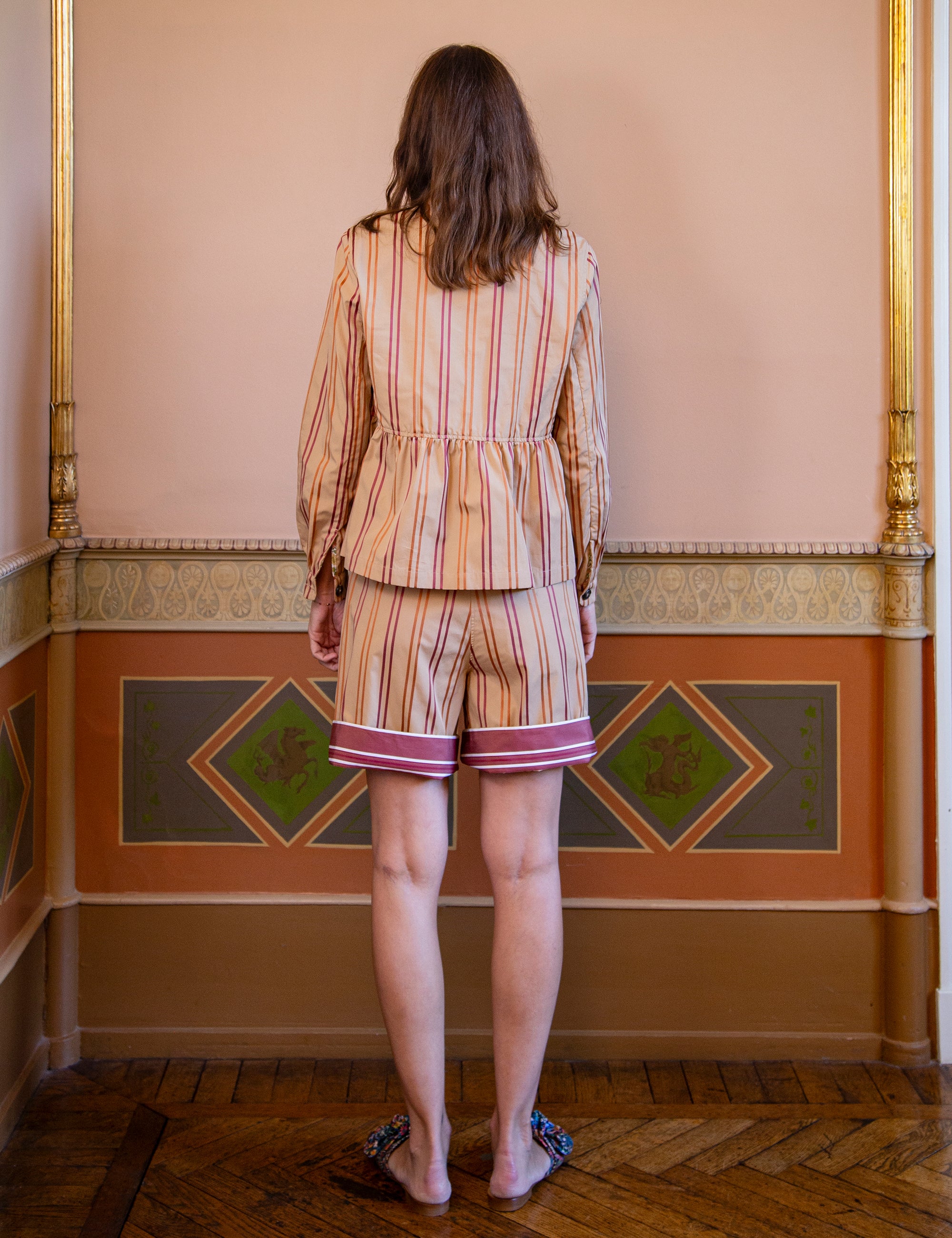 Woman in a striped jacket and shorts standing in a room with decorative walls.