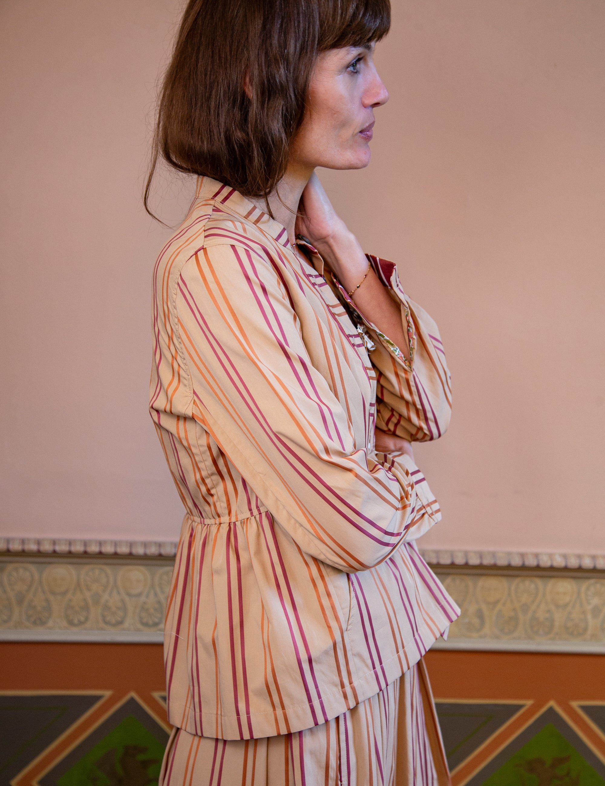 Woman wearing a striped jacket standing against a decorative wall.