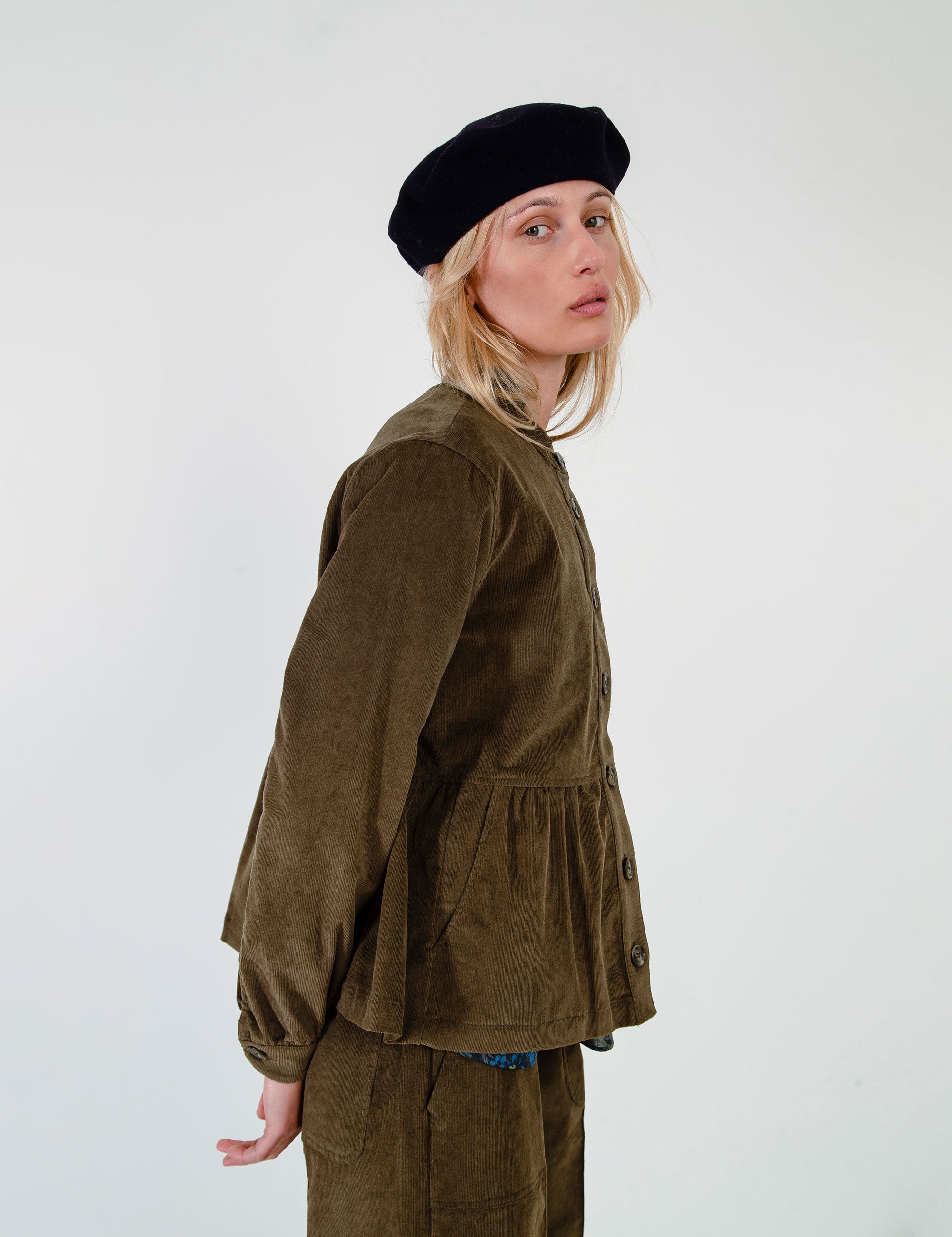 A woman wearing an olive-green corduroy jacket and matching skirt set and a black beret