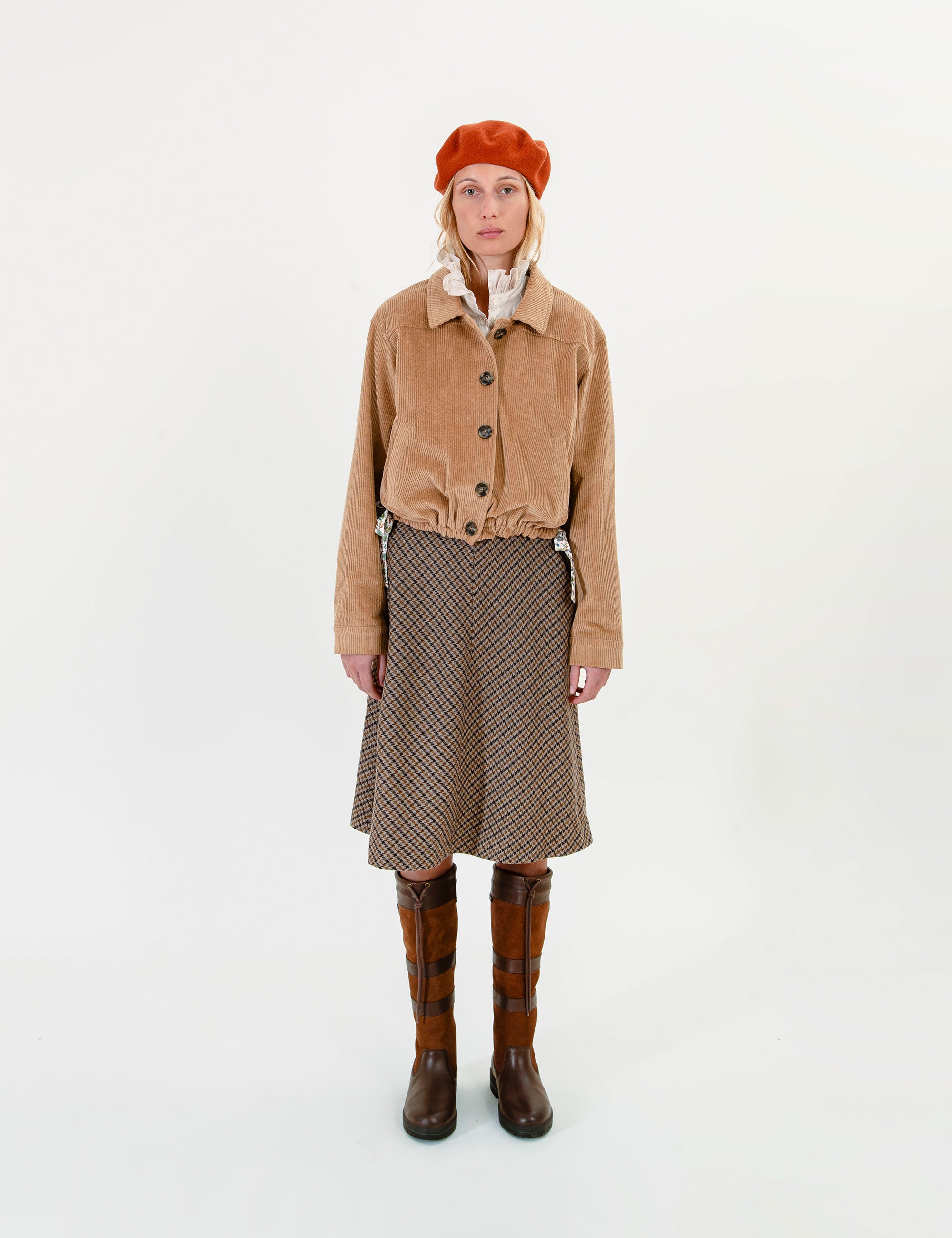 Woman wearing a tan corduroy jacket, red beret, and patterned skirt on a white background