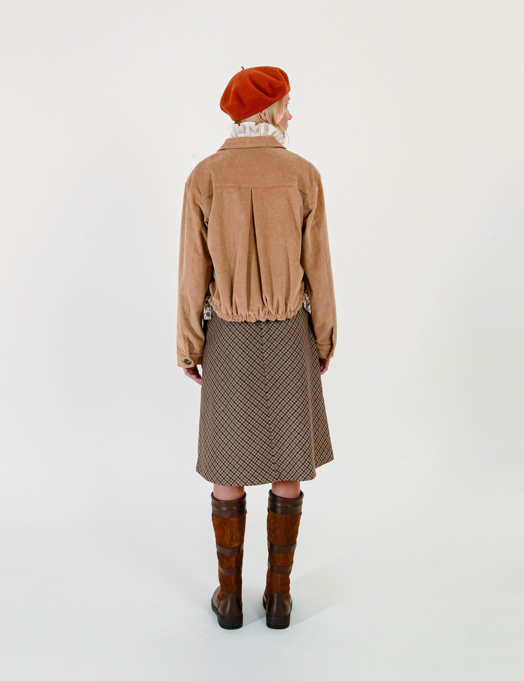 Woman wearing a tan corduroy jacket, red beret, and patterned skirt on a white background