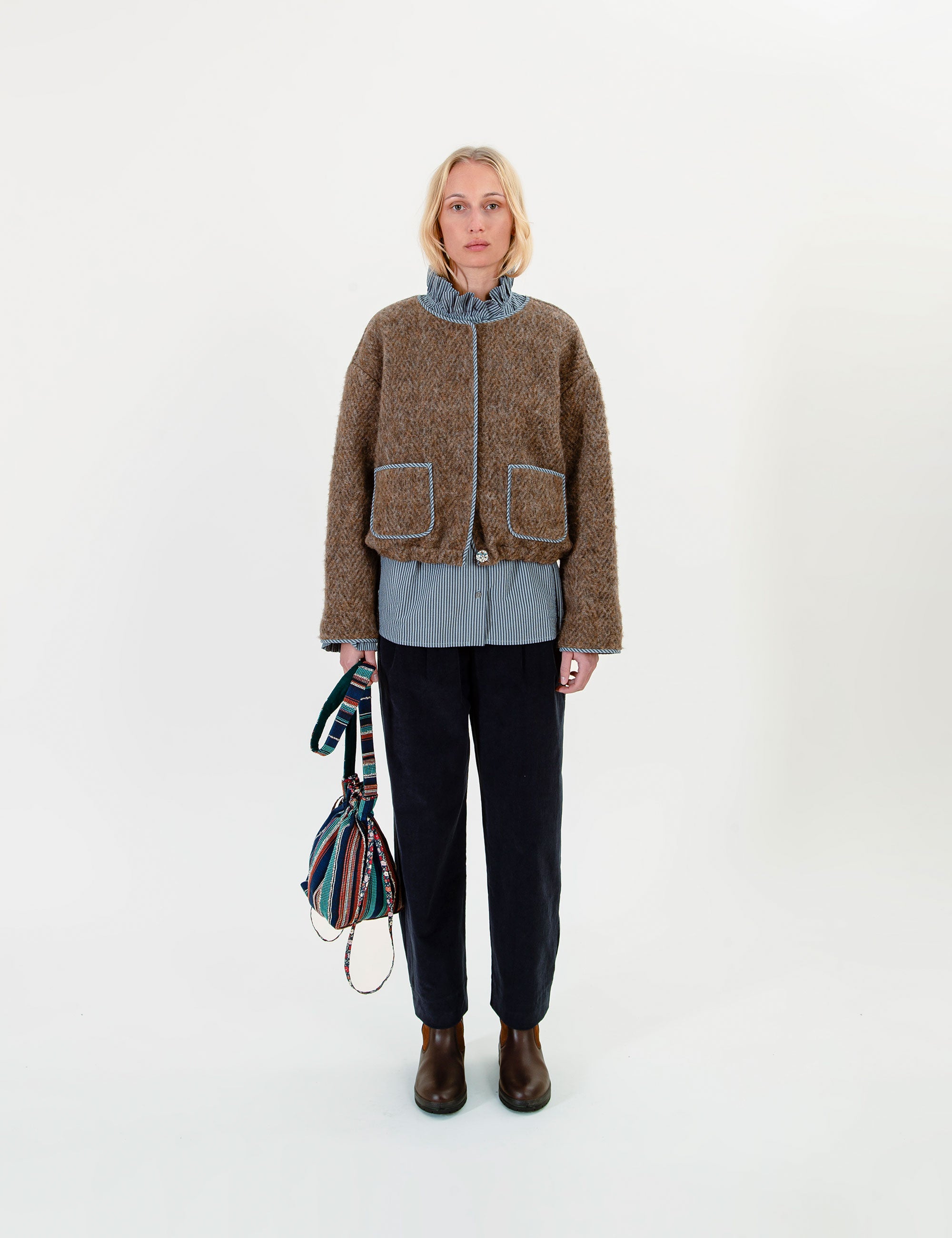 Woman wearing a brown jacket with a patterned bag on a white background