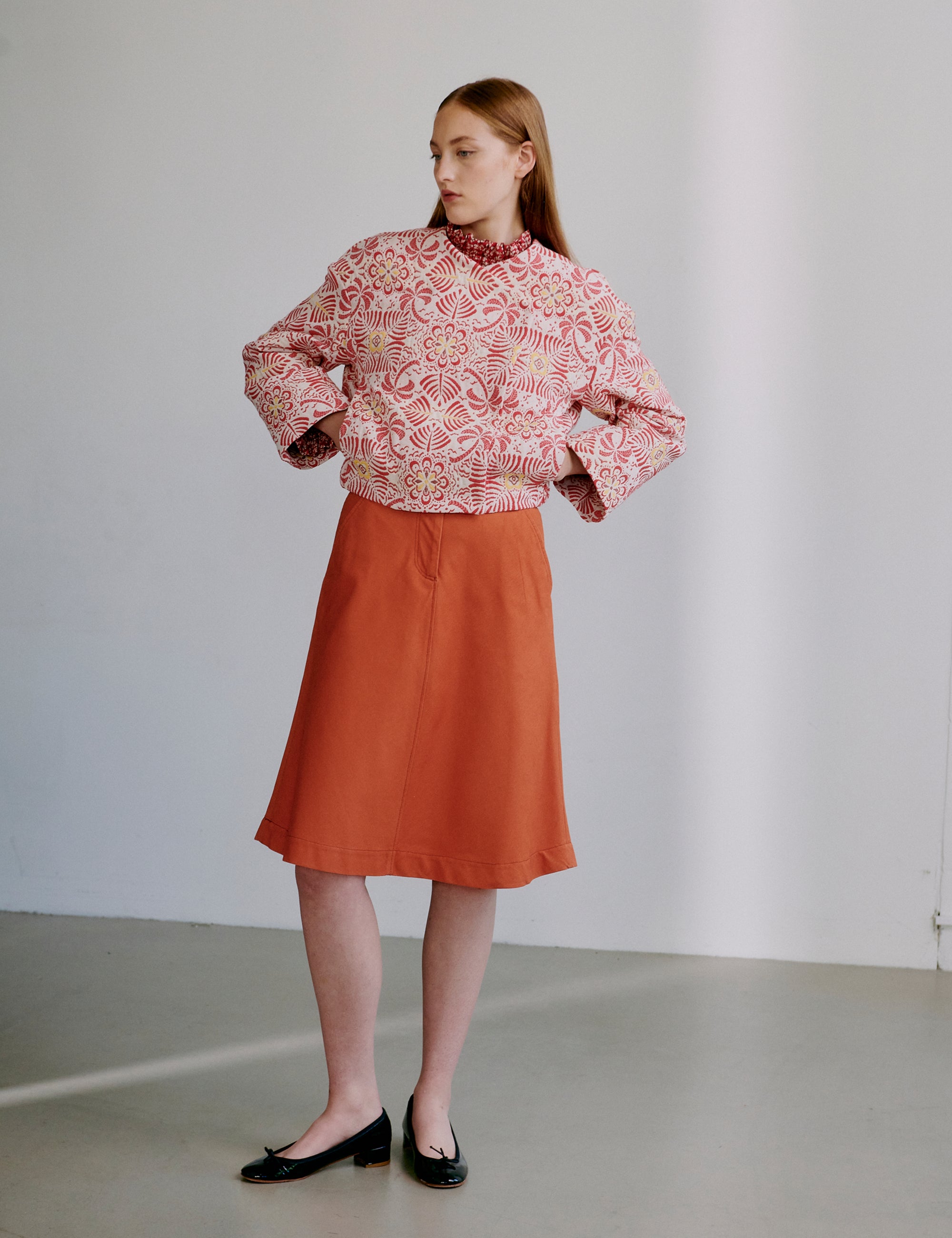 Woman wearing a red patterned jacket and orange skirt against a plain background