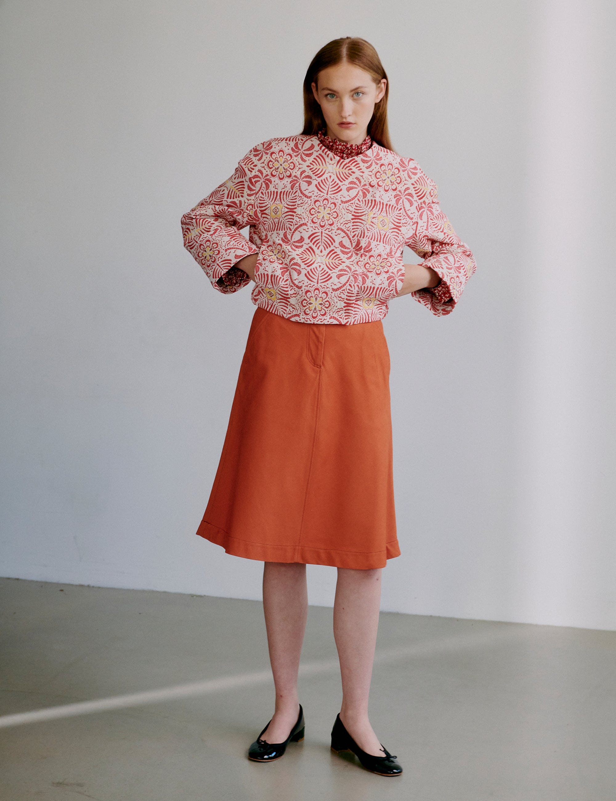 Woman wearing a red patterned jacket and orange skirt against a plain background