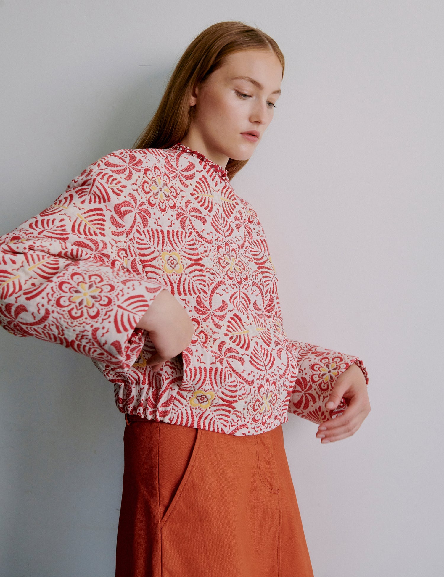 Woman wearing a red patterned jacket and orange skirt against a plain background