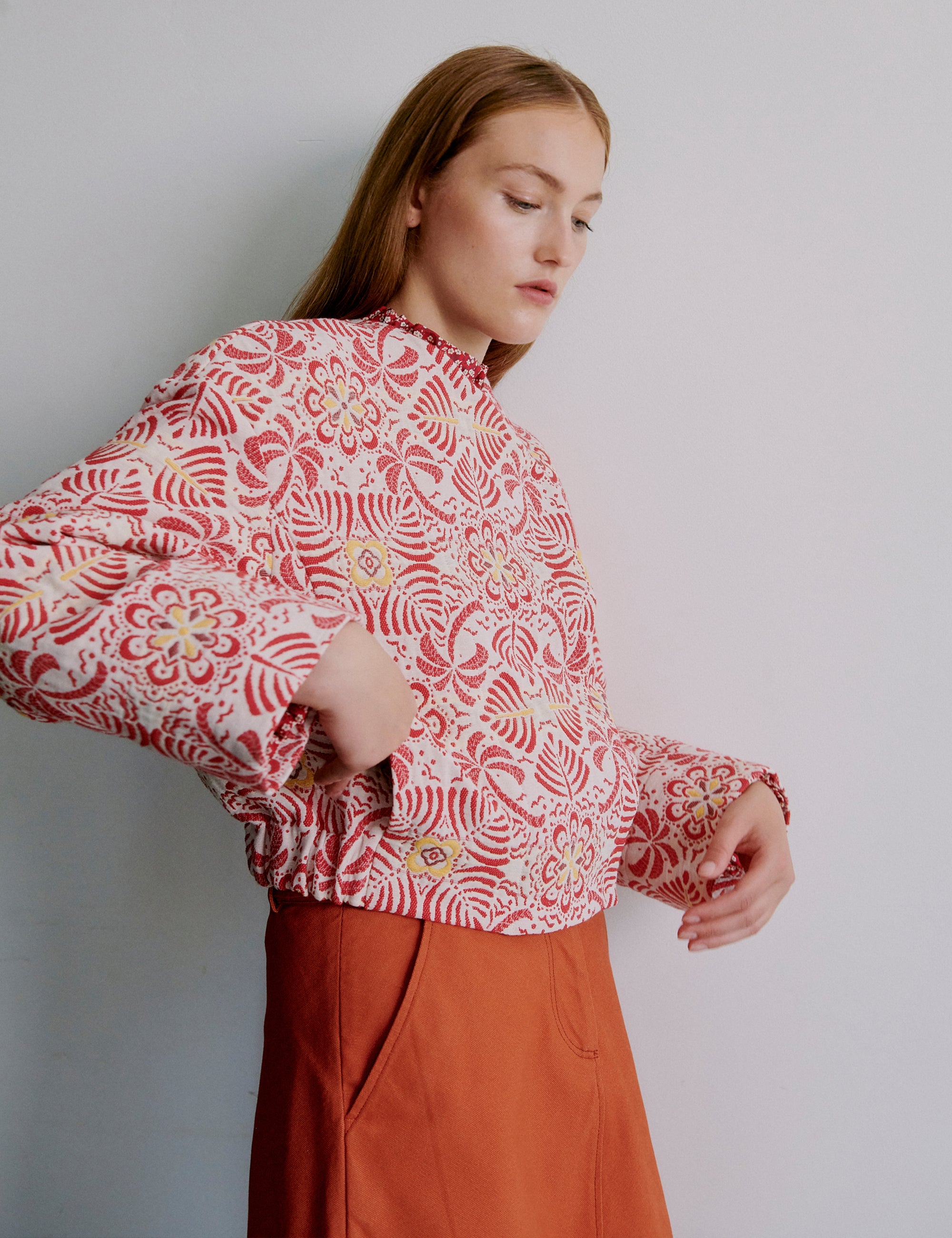 Woman wearing a red patterned jacket and orange skirt against a plain background
