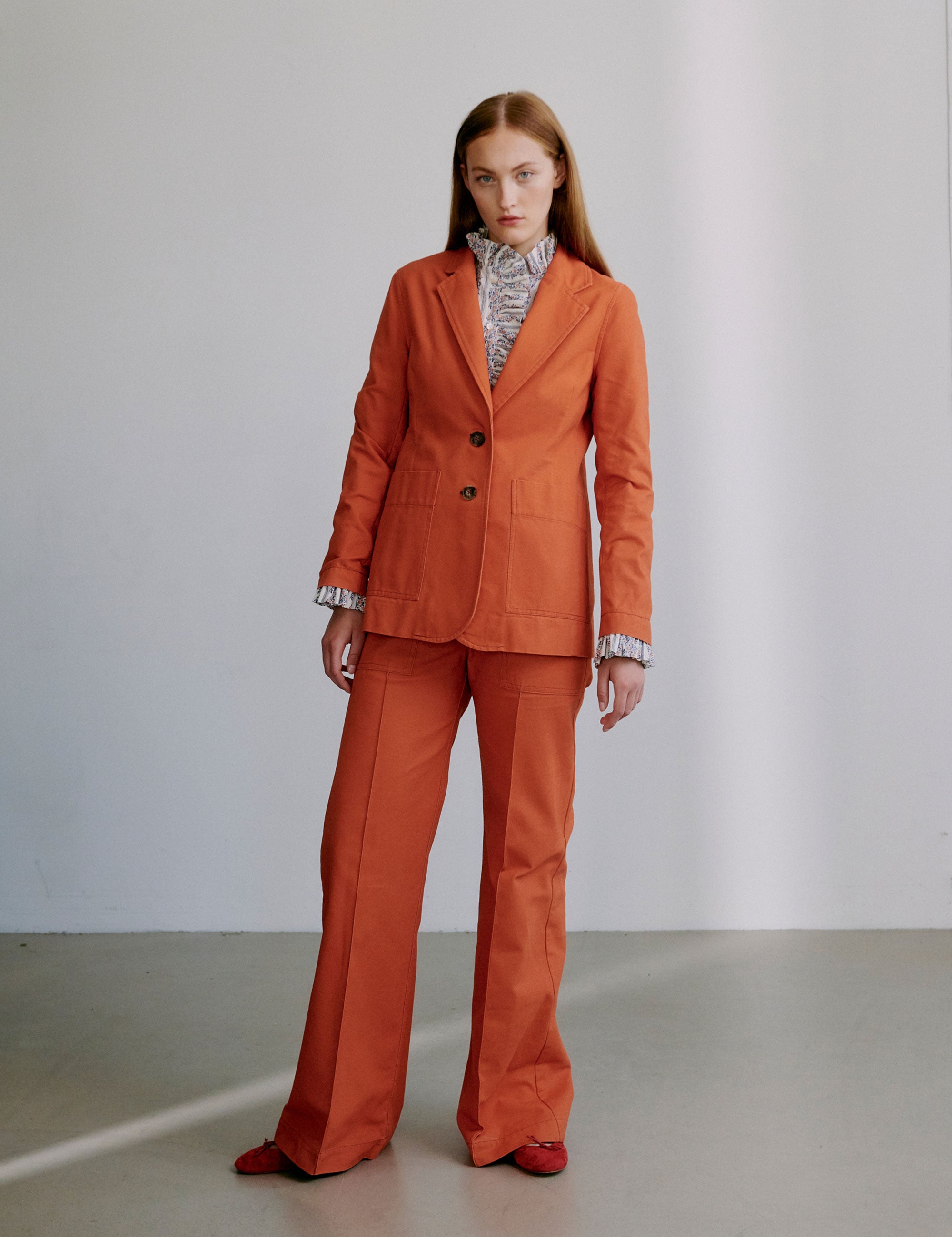 Woman wearing an orange blazer and matching pants with a frilled shirt beneath