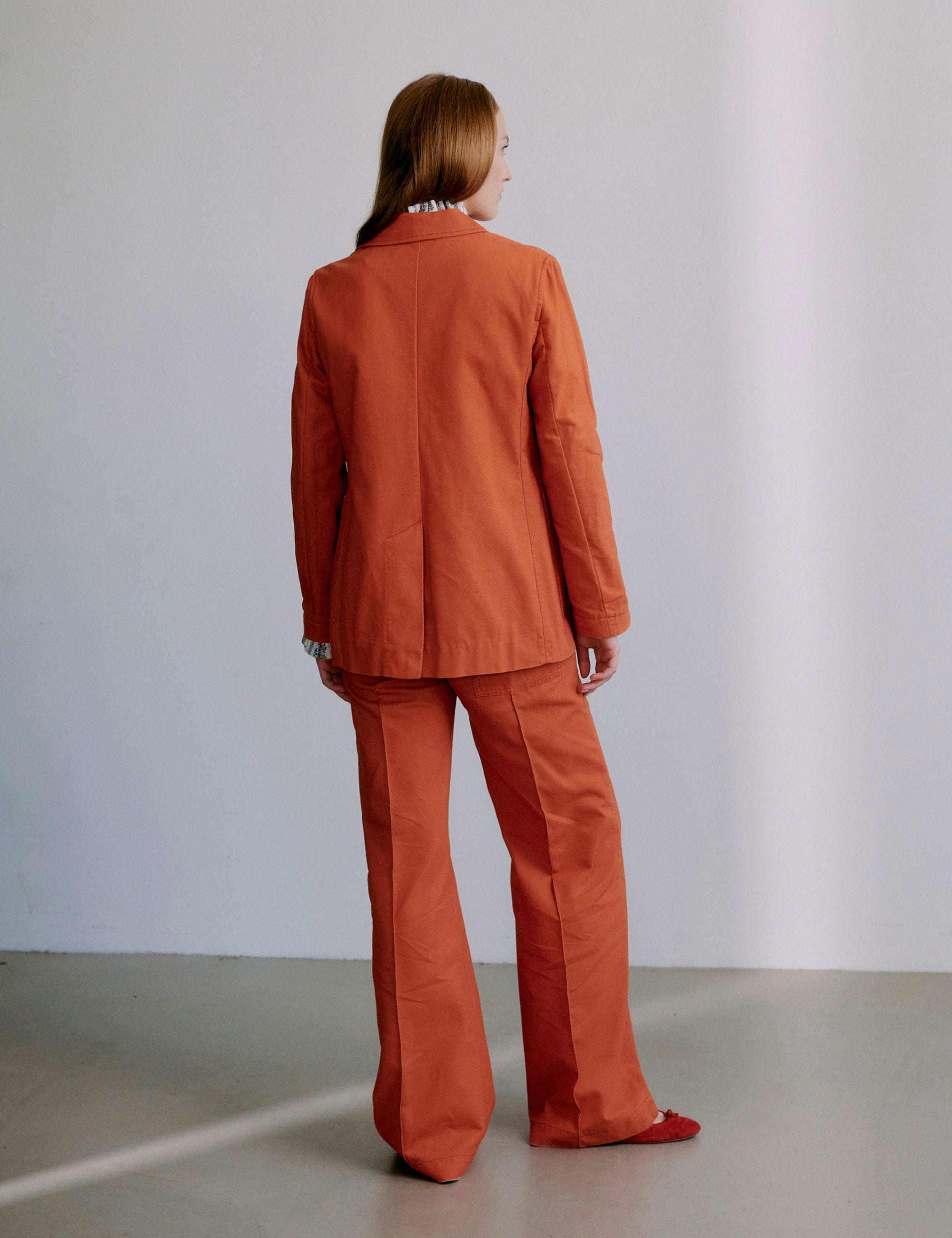 Woman wearing an orange blazer and matching pants with a frilled shirt beneath
