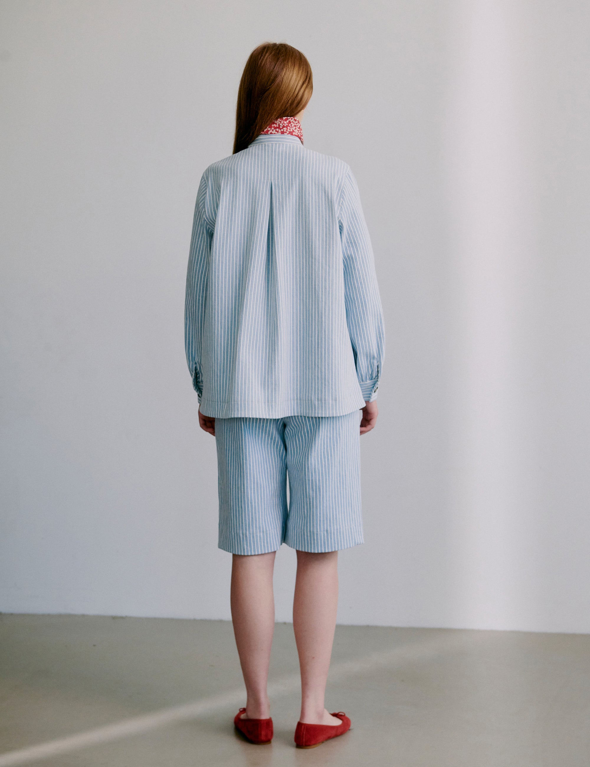 Woman wearing a light blue striped jacket with matching shorts and red shoes on a plain background