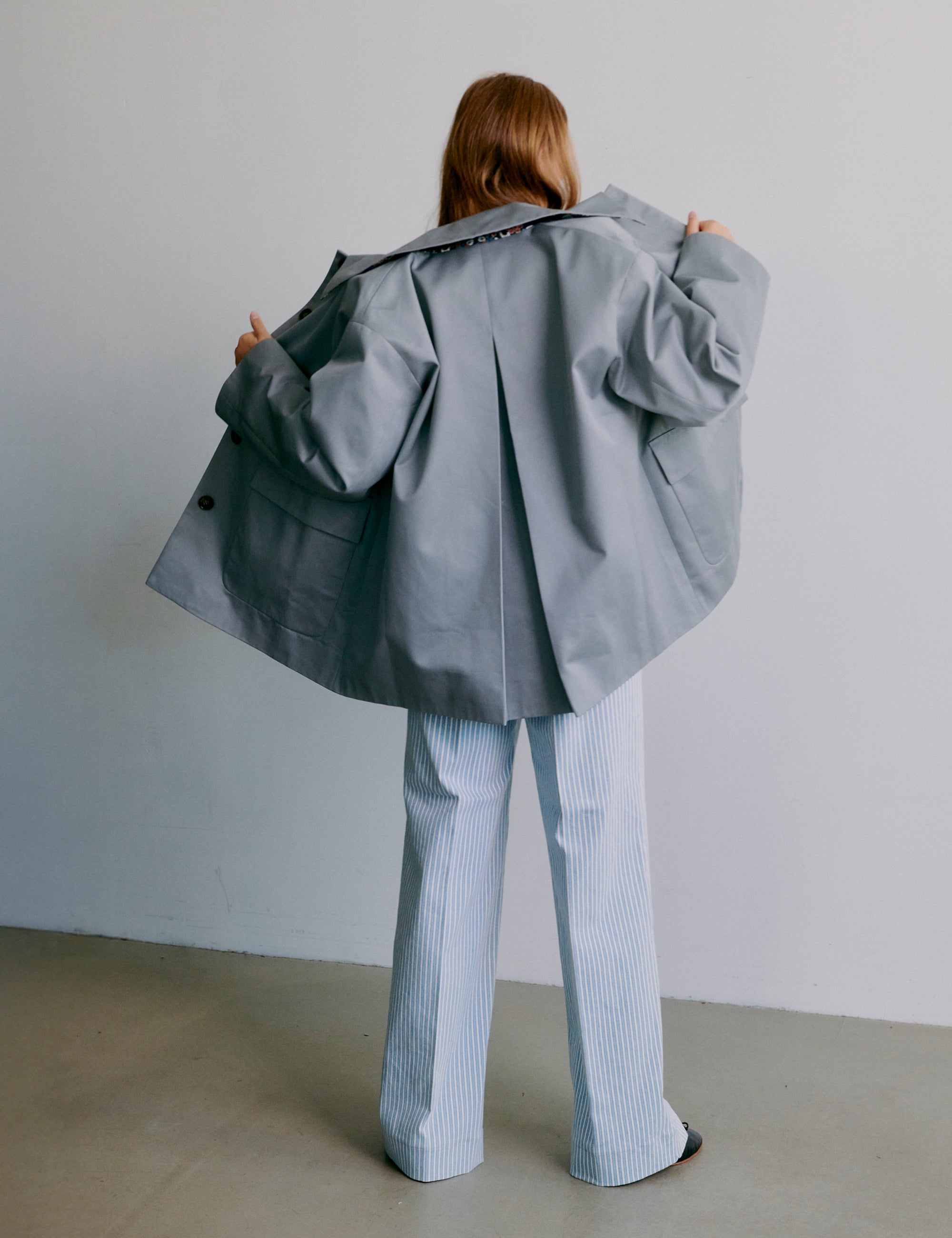 Woman wearing a gray jacket and light blue striped pants against a plain background