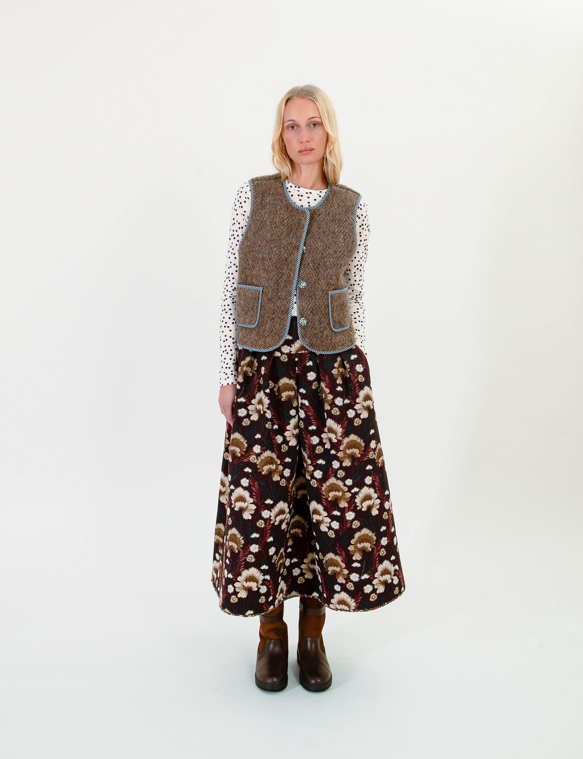 Woman wearing a patterned maxi skirt with a brown vest on a white background