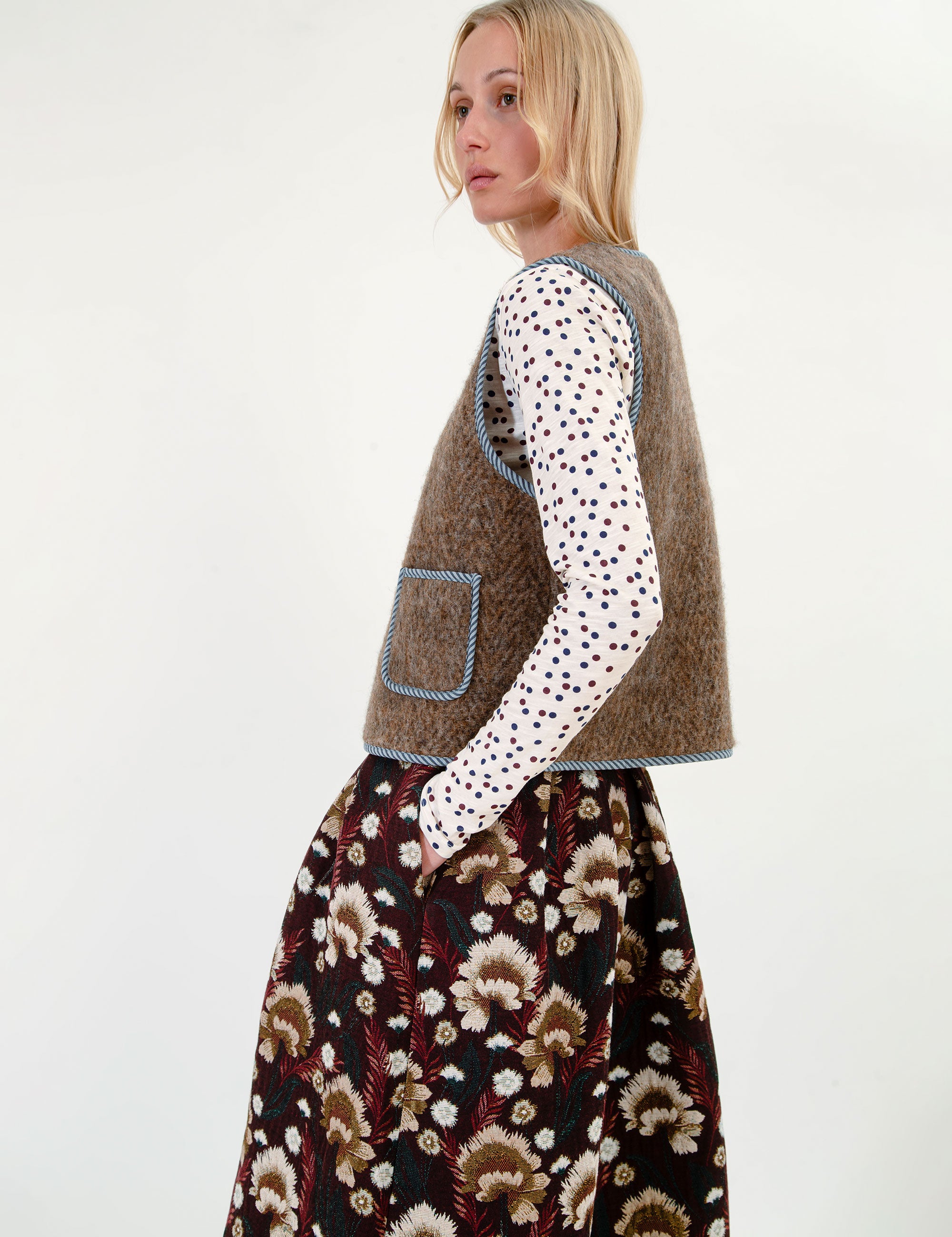 Woman wearing a patterned t-shirt, wool vest, and floral skirt on a white background