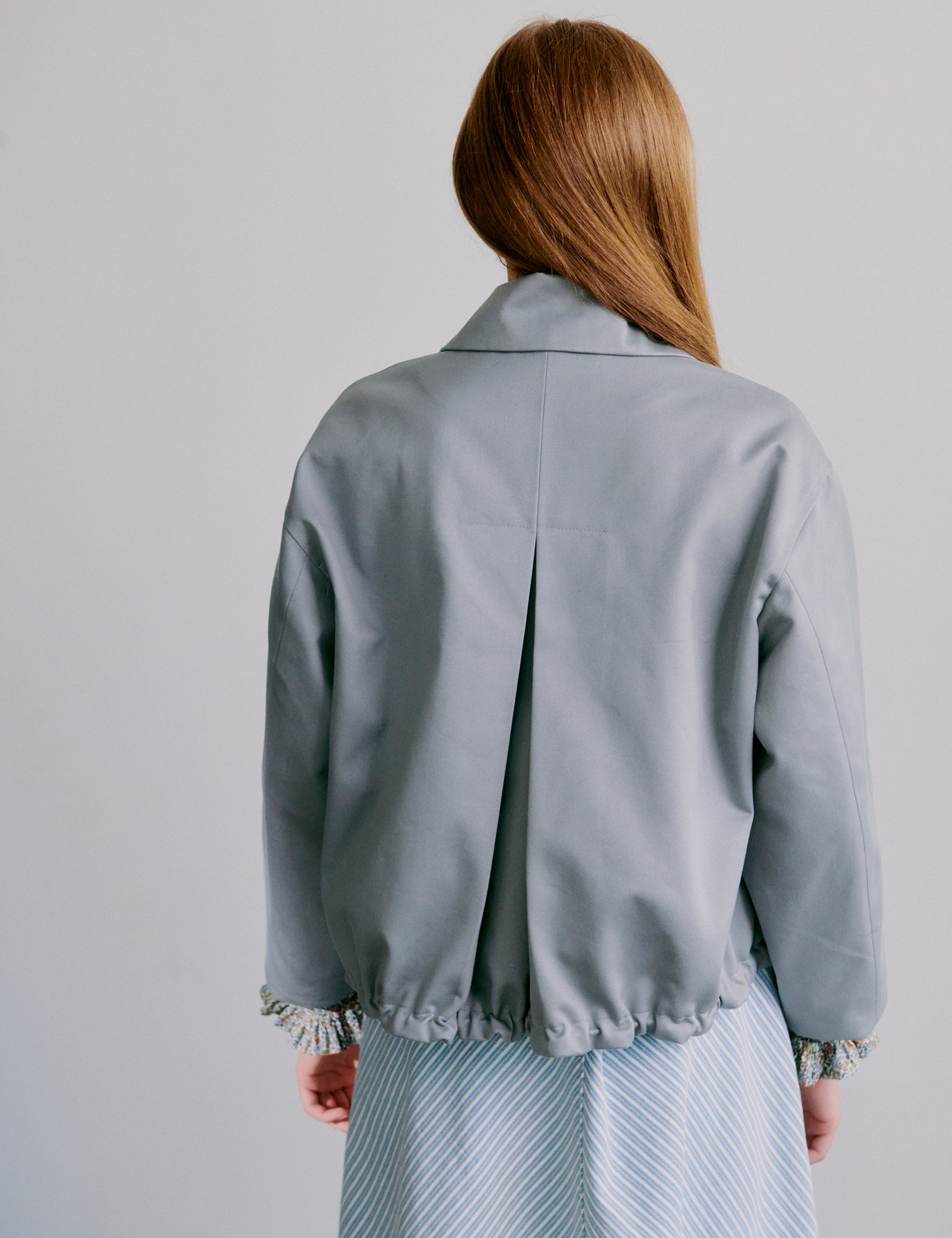 Woman wearing a light grey jacket and blue and white striped skirt