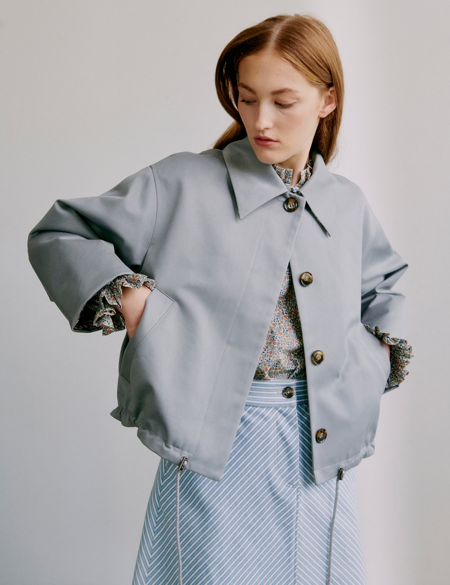 Woman wearing a light gray jacket with decorative buttons on a plain background
