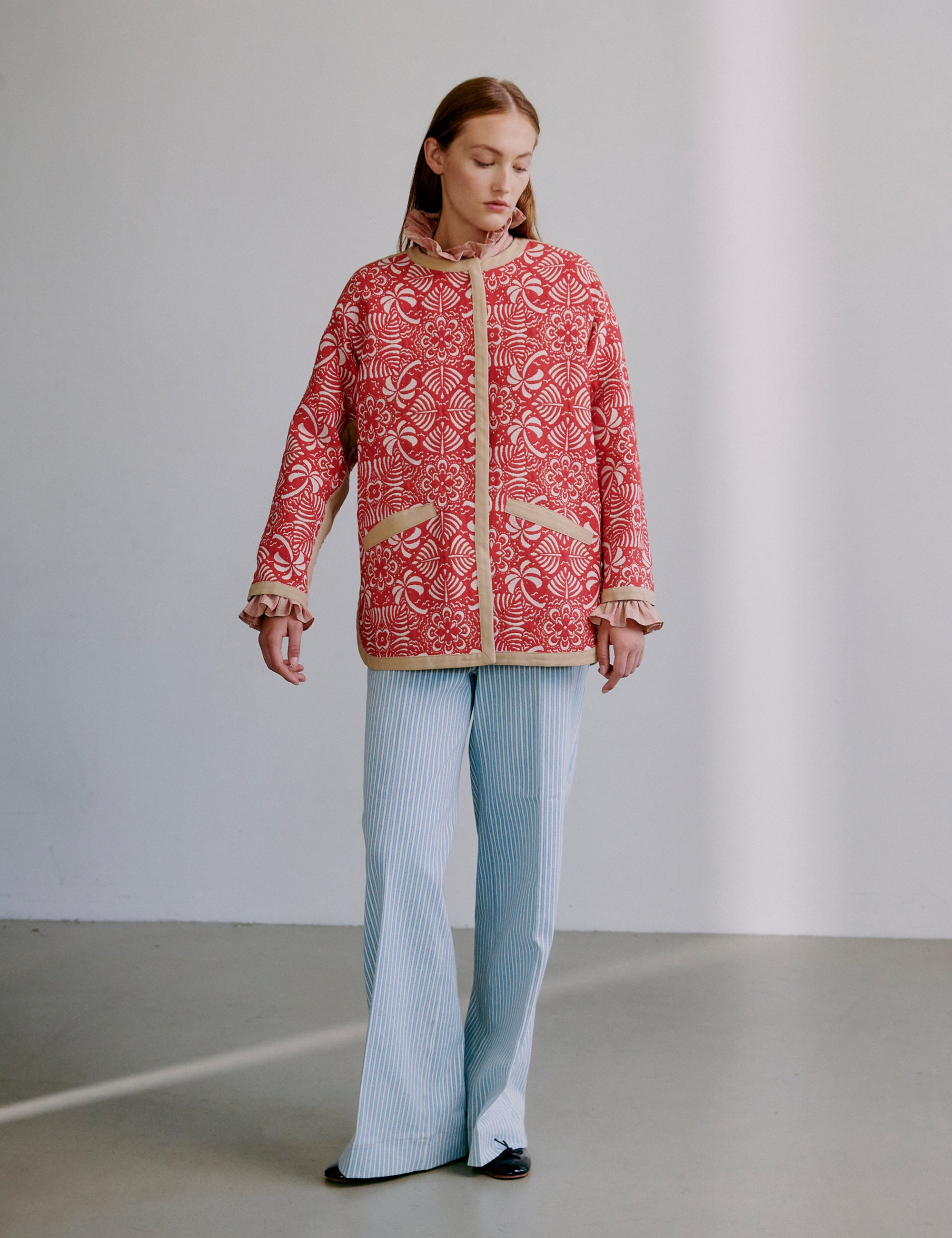Woman wearing a red patterned jacket and light blue pants against a plain background