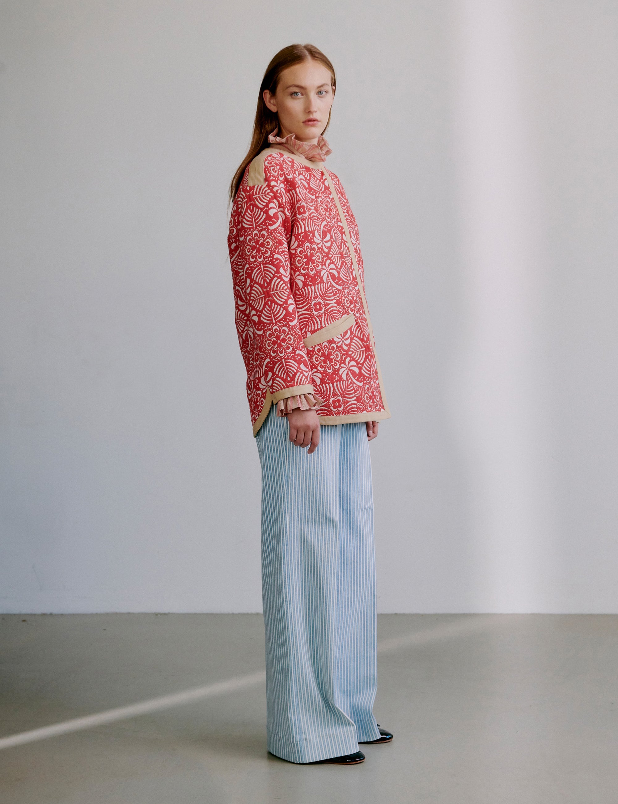 Woman wearing a red patterned jacket and light blue pants against a plain background