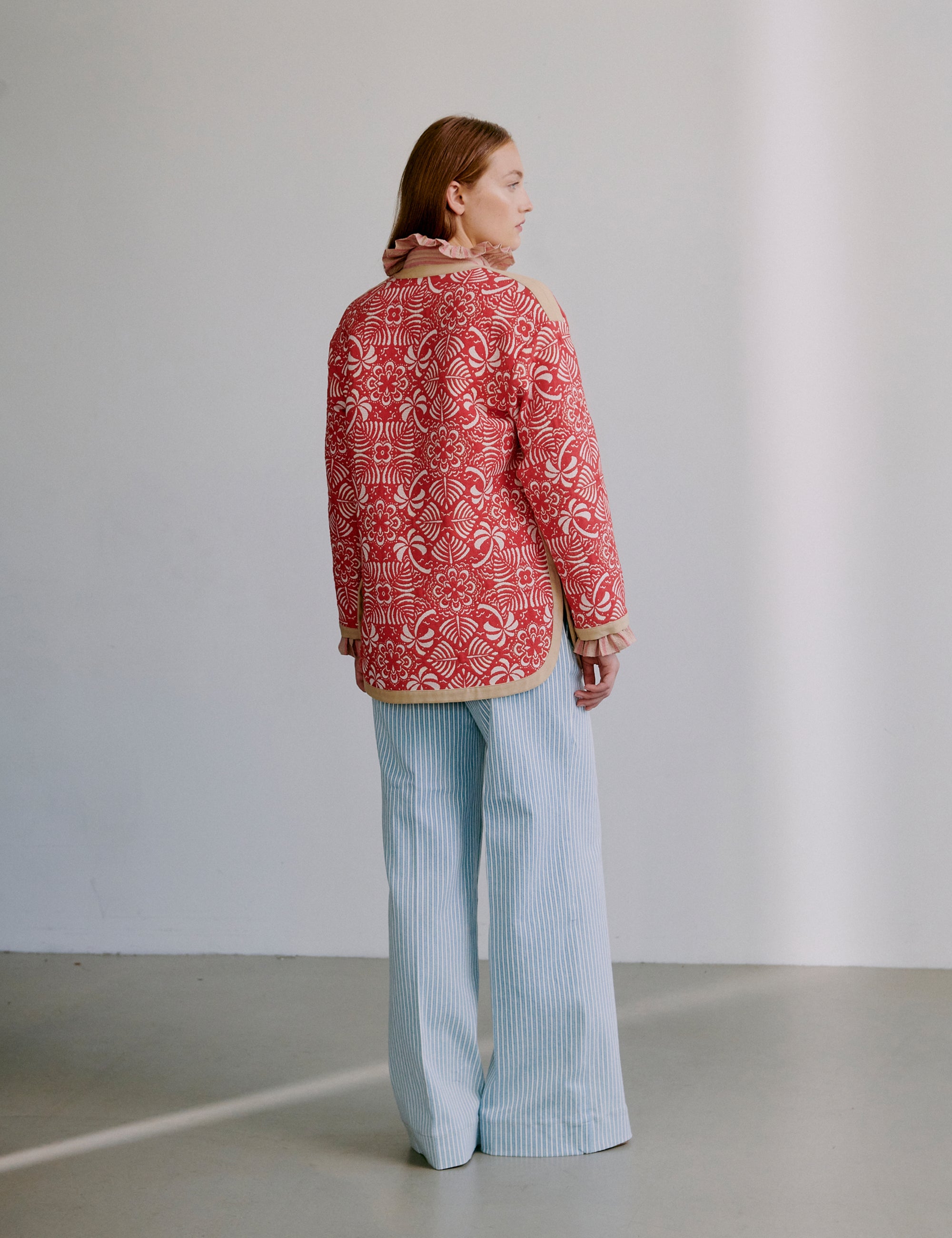Woman wearing a red patterned jacket and light blue pants against a plain background