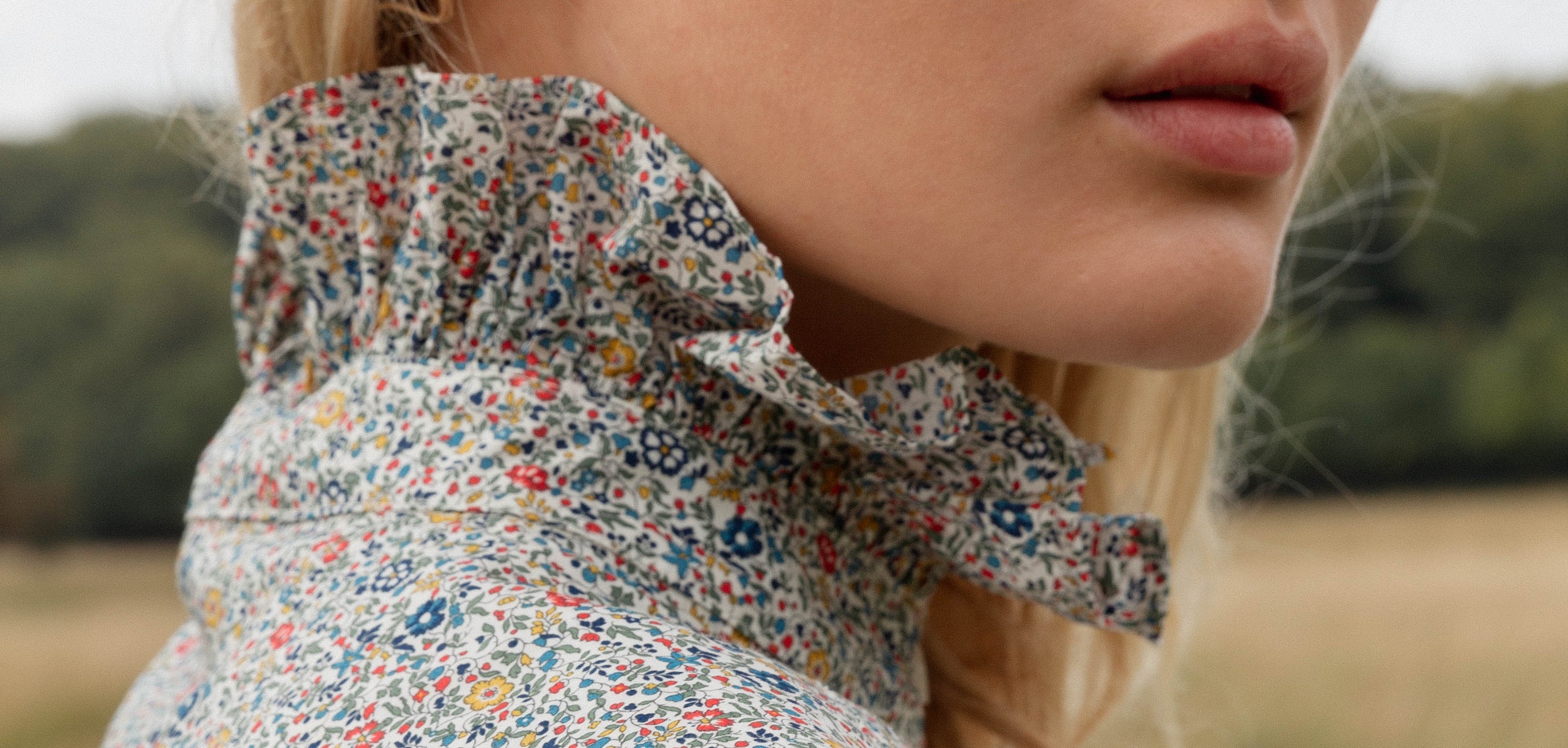 Close-up of a woman wearing an APOF  floral blouse with ruffled collar on a blurred natural background
