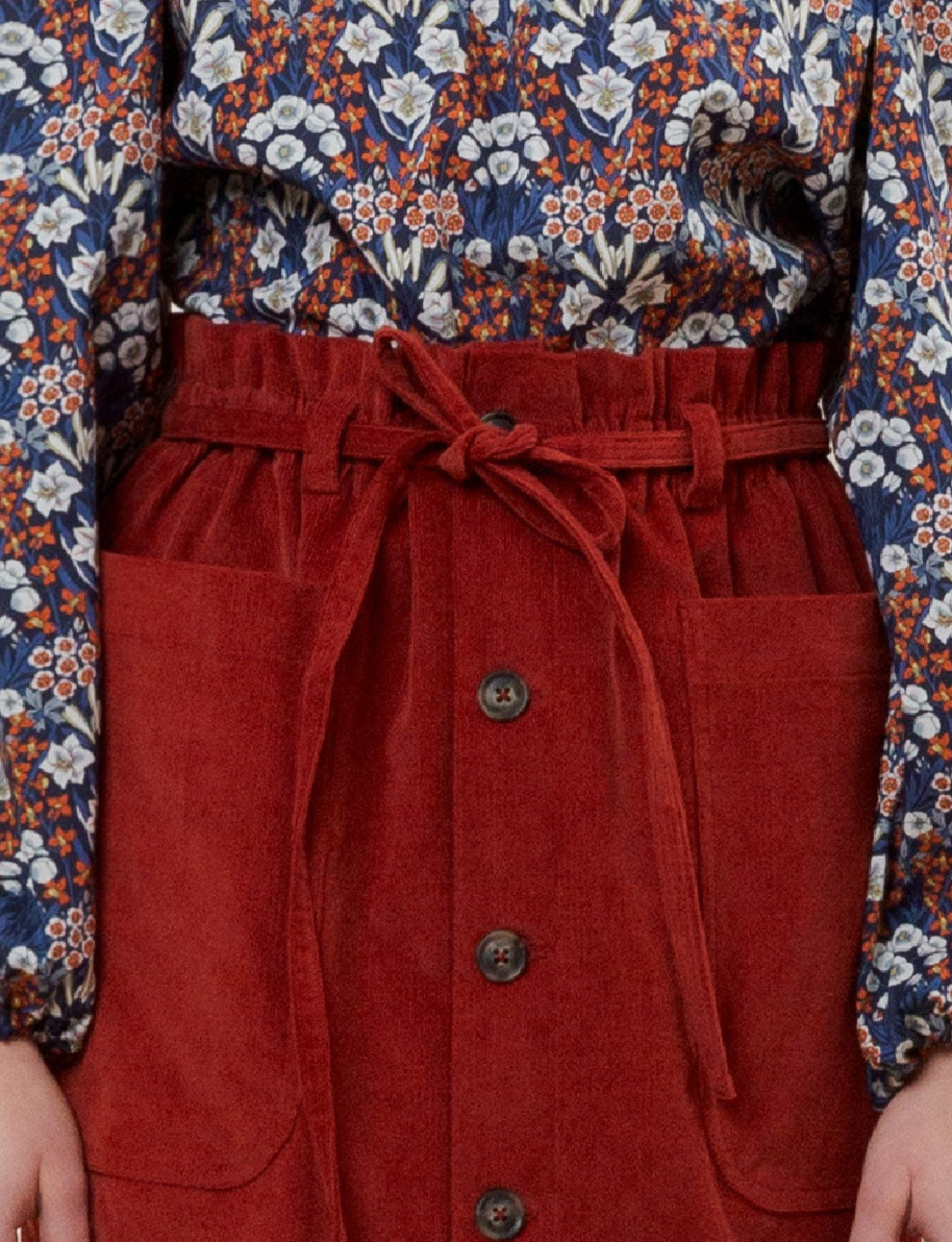 Red corduroy skirt with buttons and strings and red blue and white flower patterned blouse