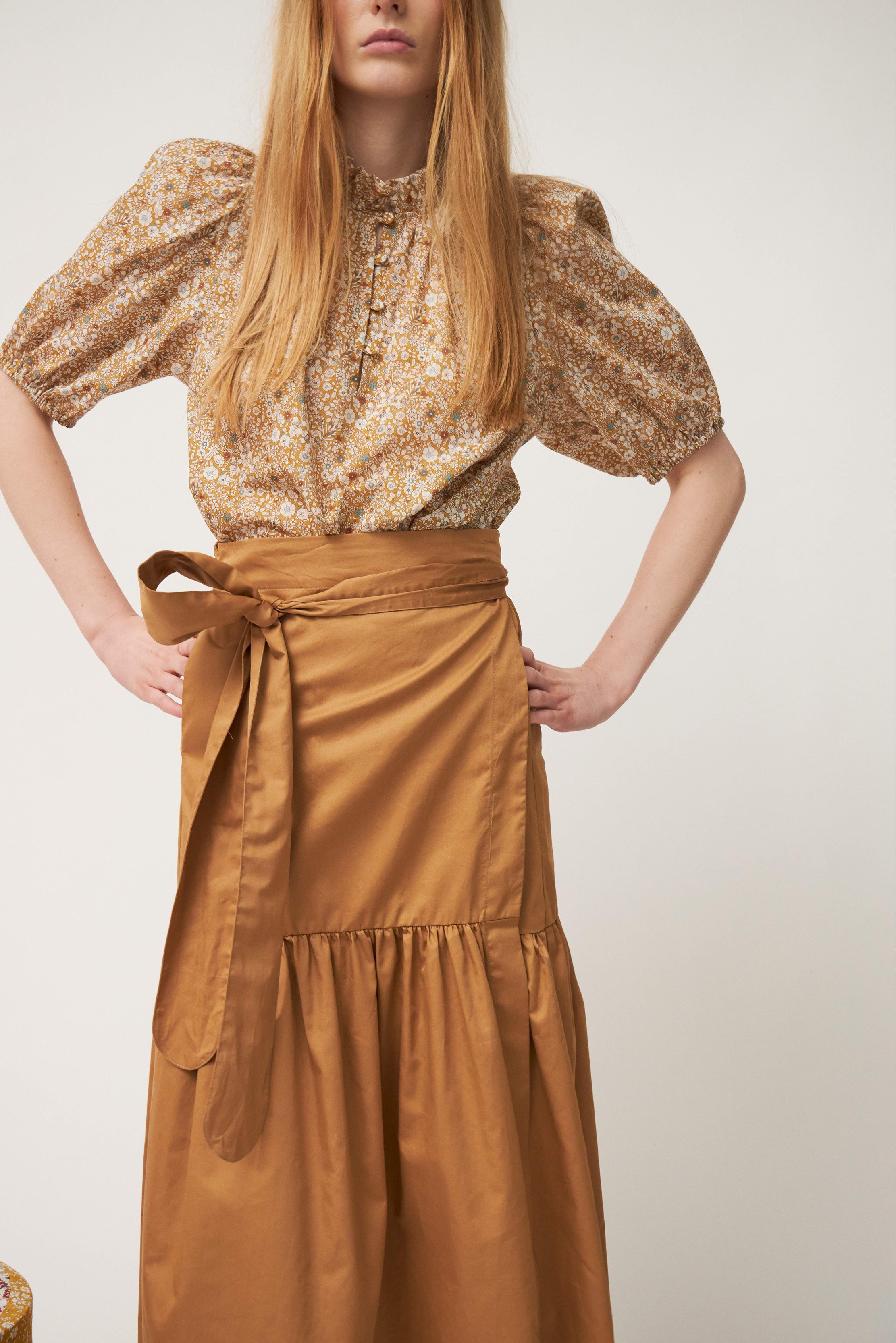 Woman in biscuit brown wrap skirt and short sleeved flower patterned shirt