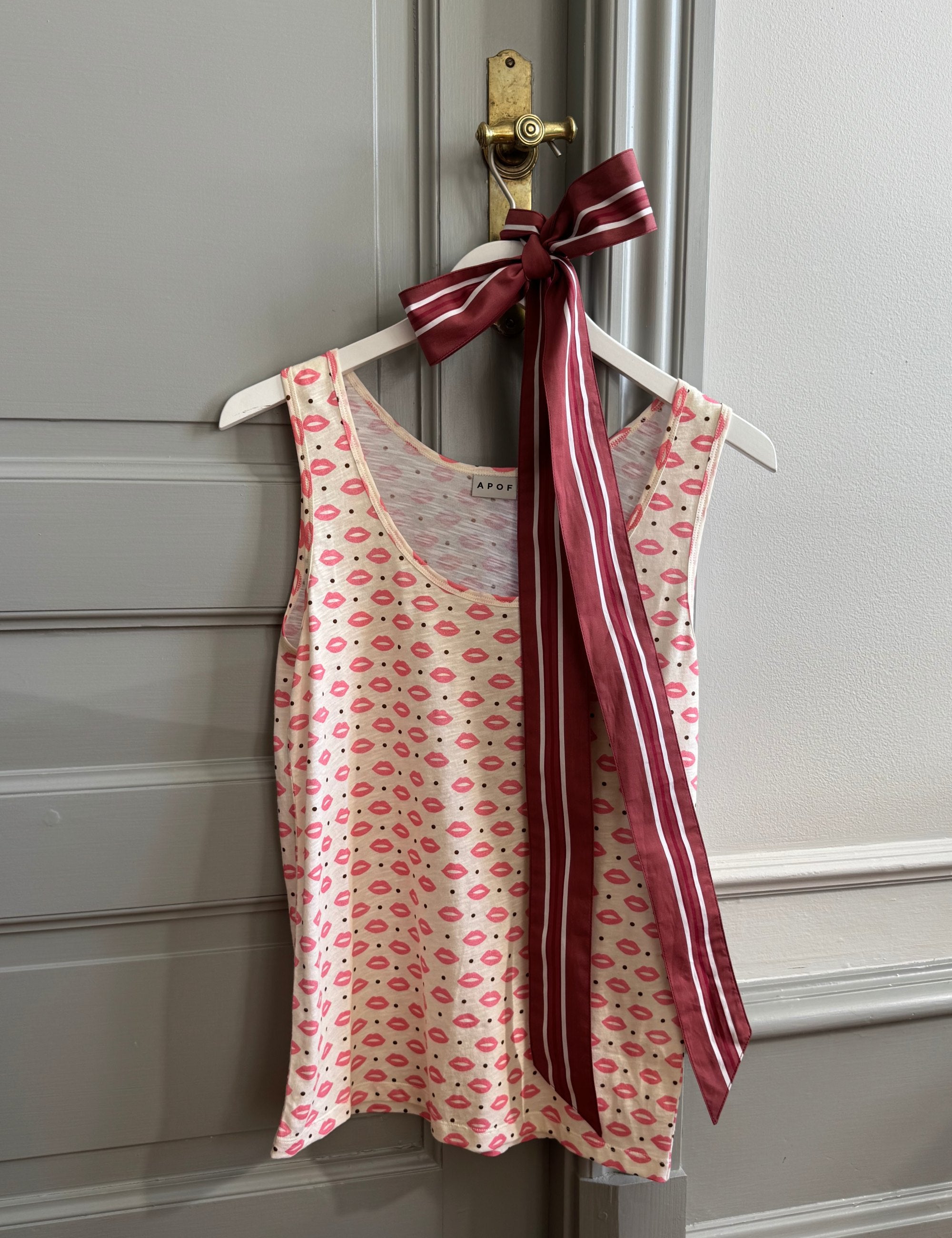 Tank top with pink kisses print and red striped fabric hanging on a door handle.