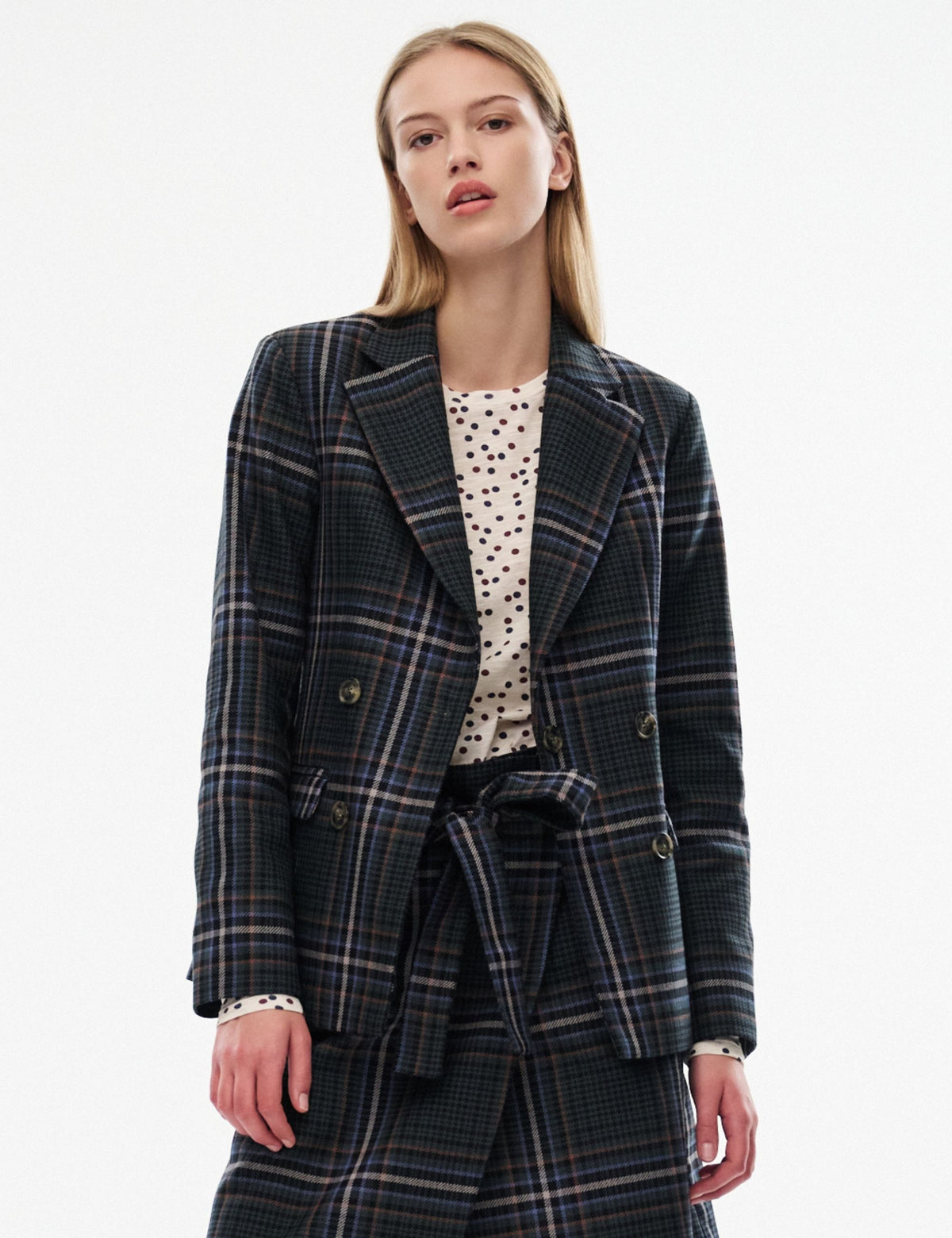 Model wearing a dark blue checked blazer and matching trousers with a cream polka-dot top against a white background.