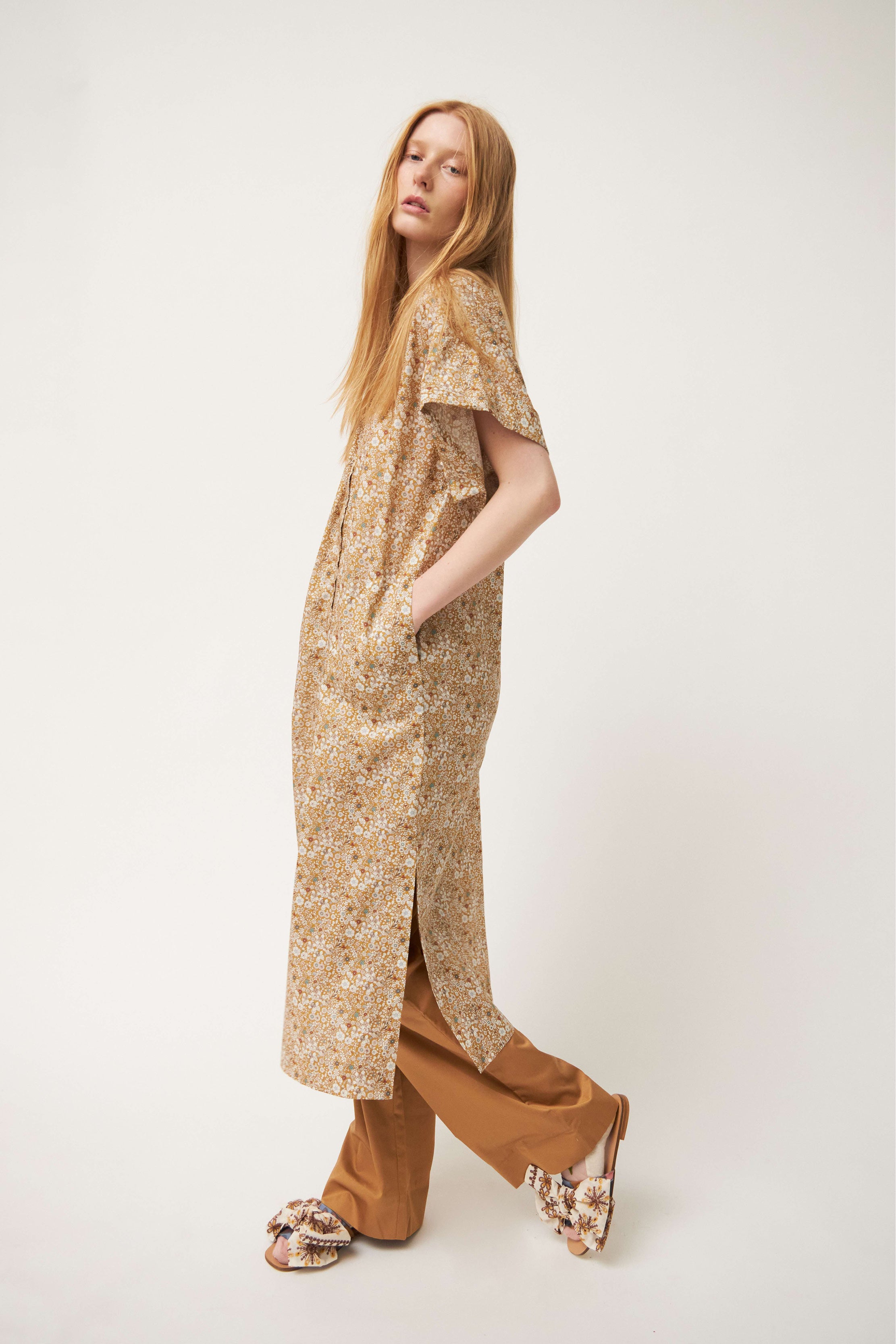 Woman in brown cotton pants with strap and pockets, flower print tunic dress and sandals with bows