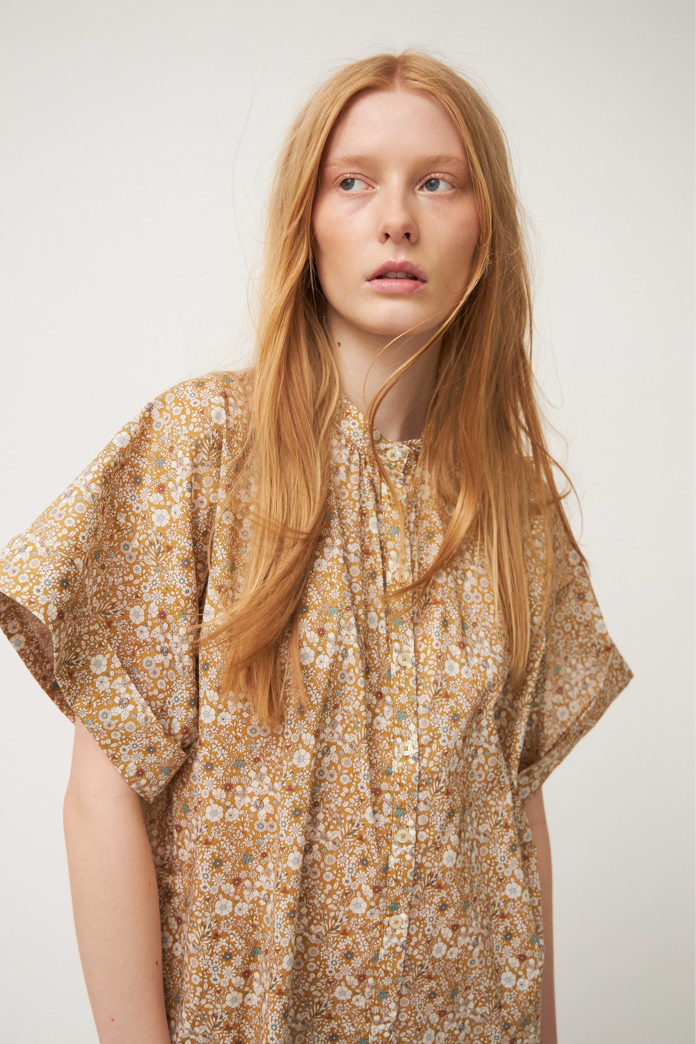 Model wearing white and brown flower patterned kaftan dress with short sleeves and buttons