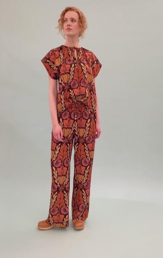 Woman in viscose pants and short sleeved top with large floral pattern in pink orange and yellow